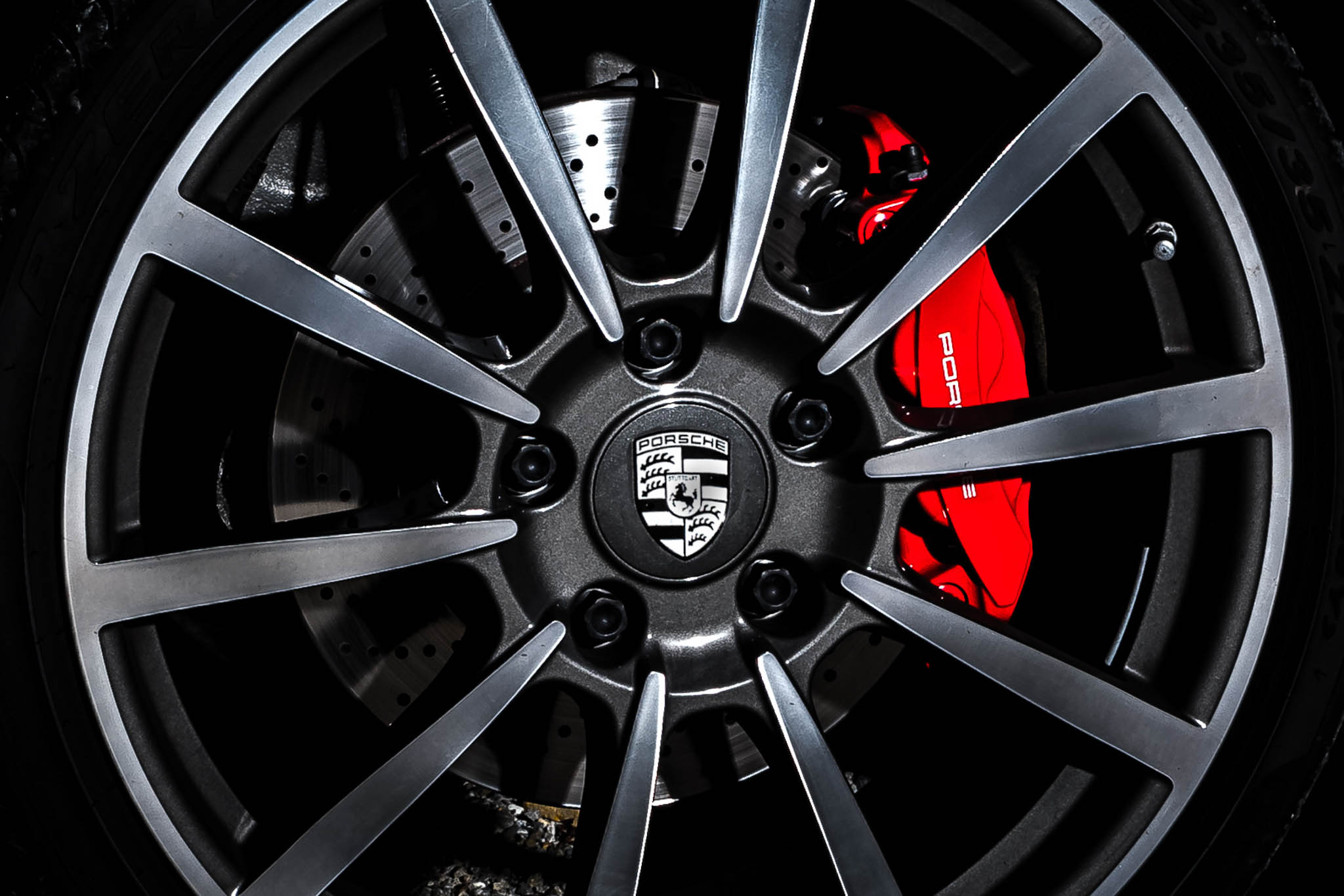 Close-up of a Porsche wheel with metallic spokes and red brake caliper, showcasing sleek automotive design.