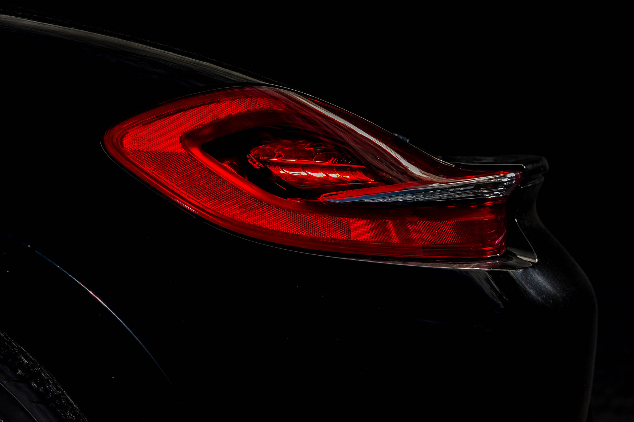 Sleek red car taillight on a black vehicle against a dark background.