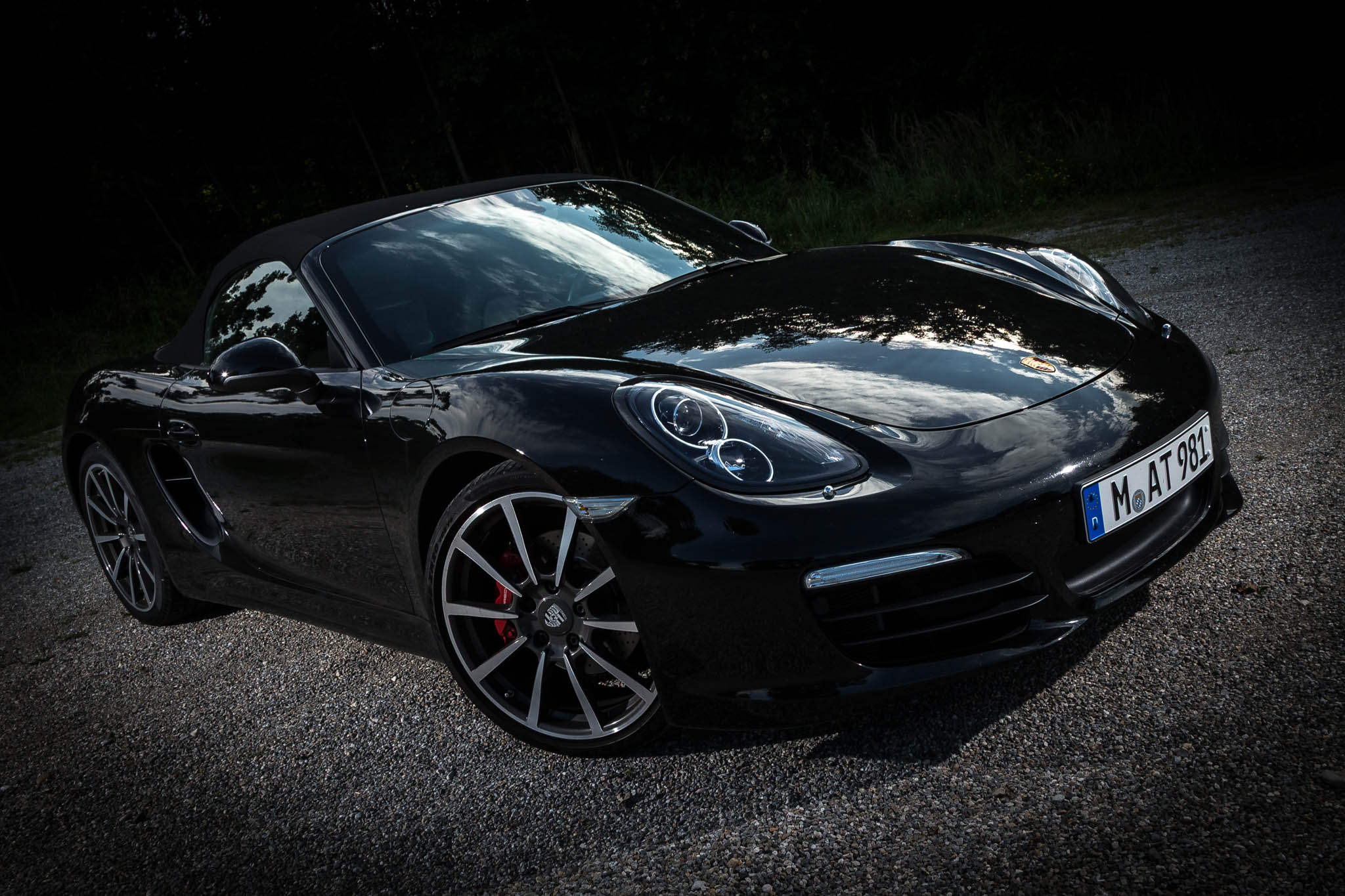 Sleek black convertible sports car parked on gravel with a reflective hood and stylish alloy wheels.