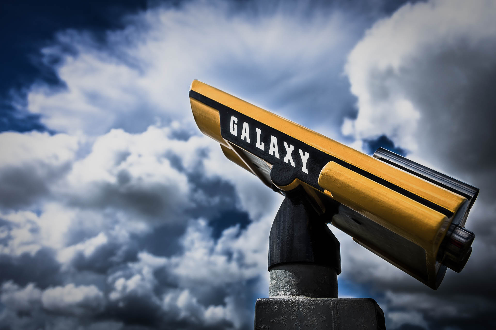 Yellow telescope labeled GALAXY against a dramatic cloudy sky.