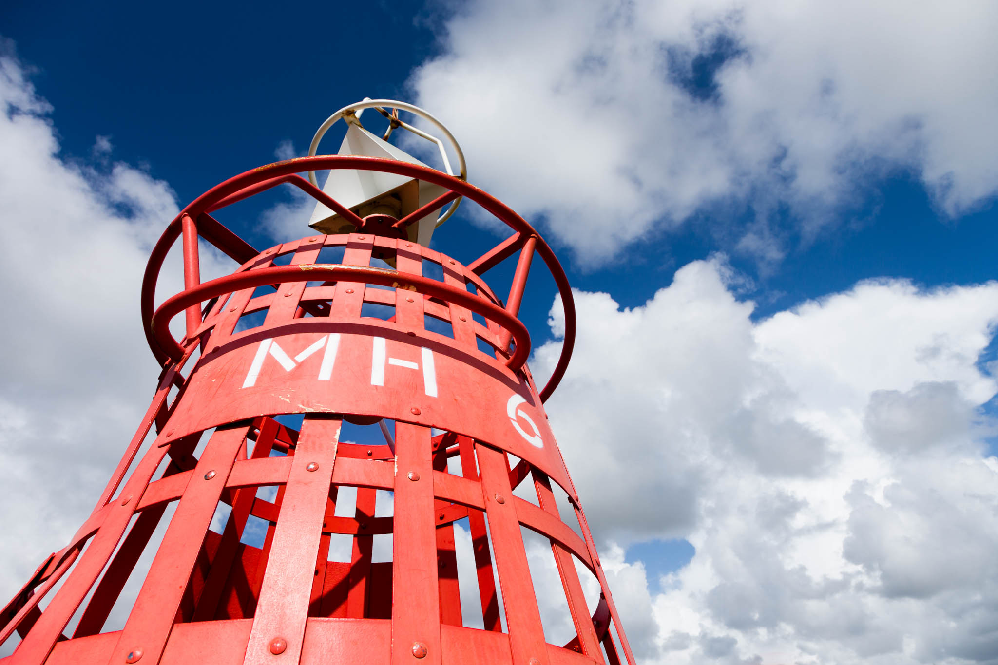 Red metal structure with MH 6 against a blue sky with clouds.