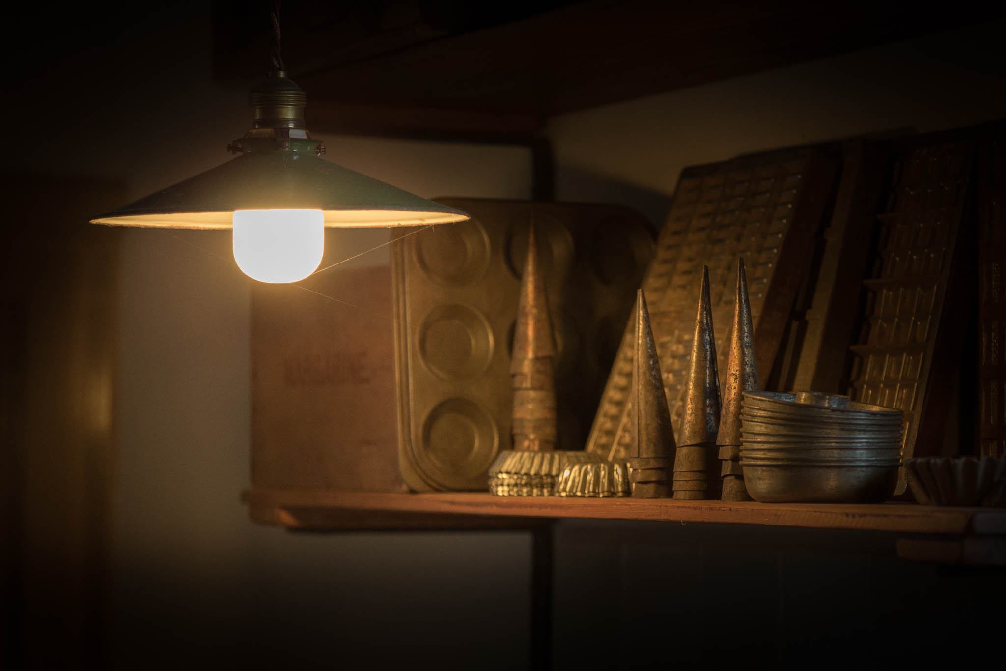Vintage kitchen molds on a shelf lit by a warm light bulb, creating a cozy, nostalgic atmosphere.