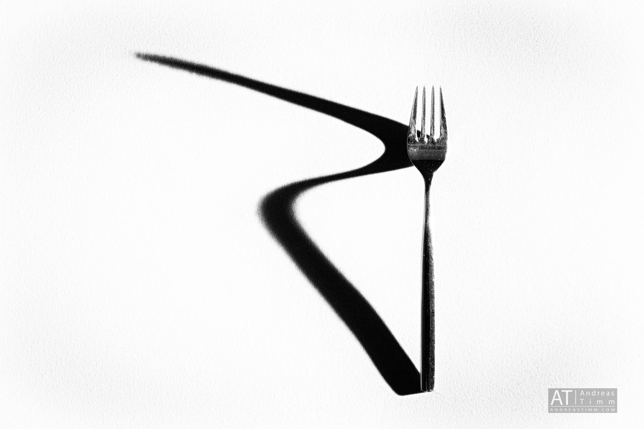Fork casting a long zigzag shadow on a white surface, creating a striking minimalist composition.
