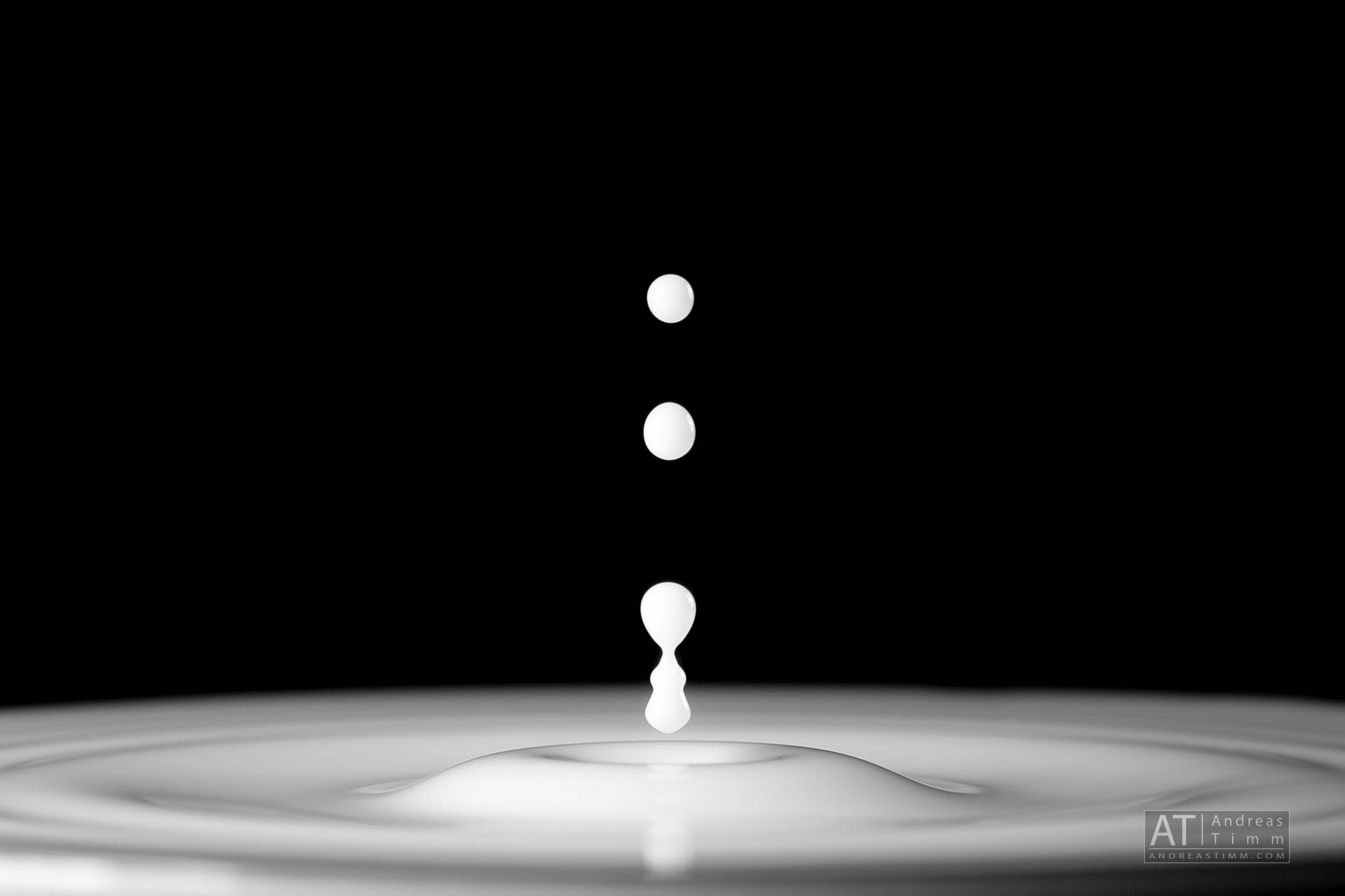 Milk droplets falling and creating ripples on a smooth surface against a black background.