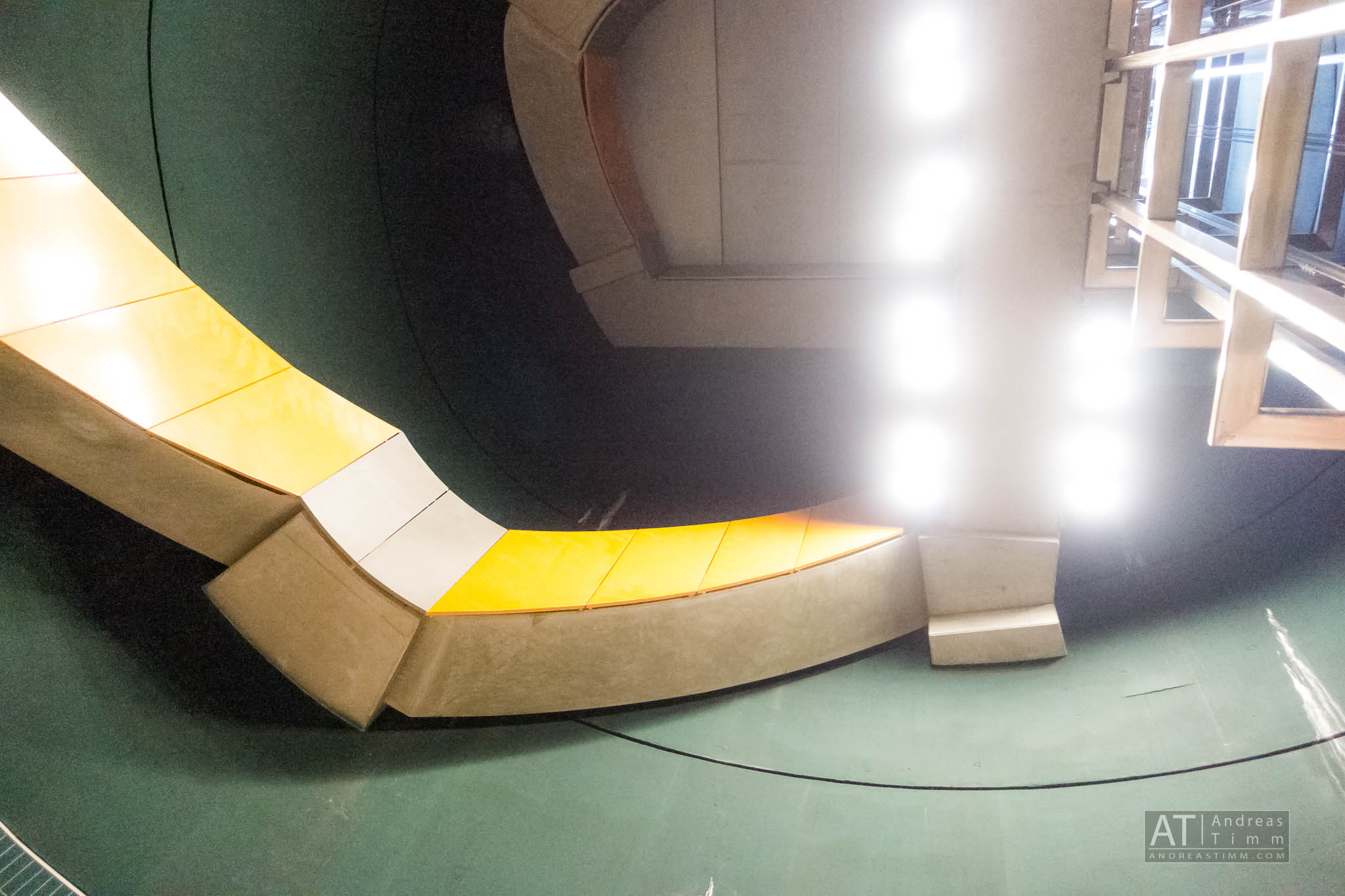 Curved architectural structure with bright lights and geometric patterns on the ceiling, featuring yellow panels.