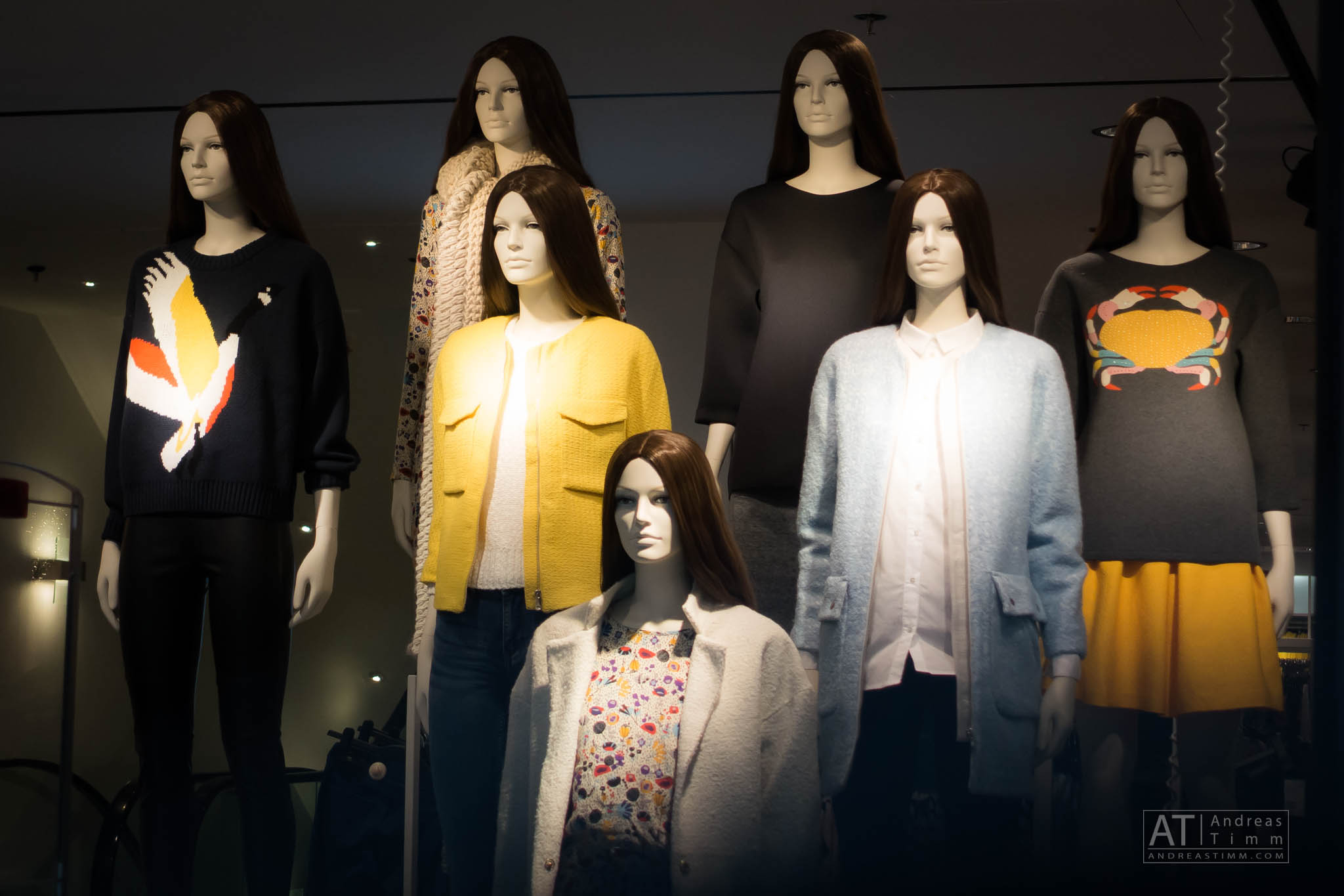 Mannequins display stylish fall sweaters with unique patterns and vibrant colors in a store window.