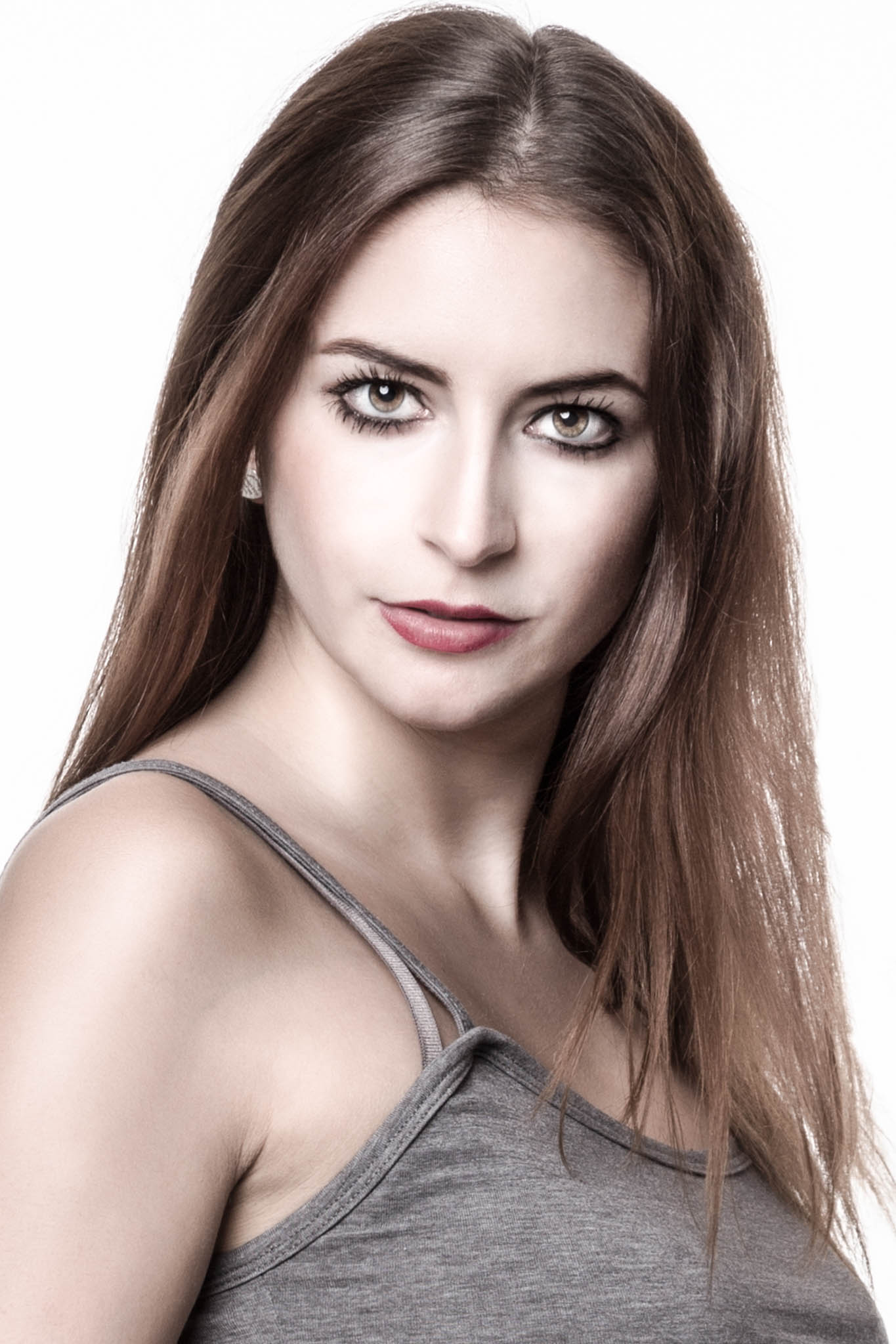Close-up of a woman with long brown hair and intense gaze, wearing a gray tank top against a white background.