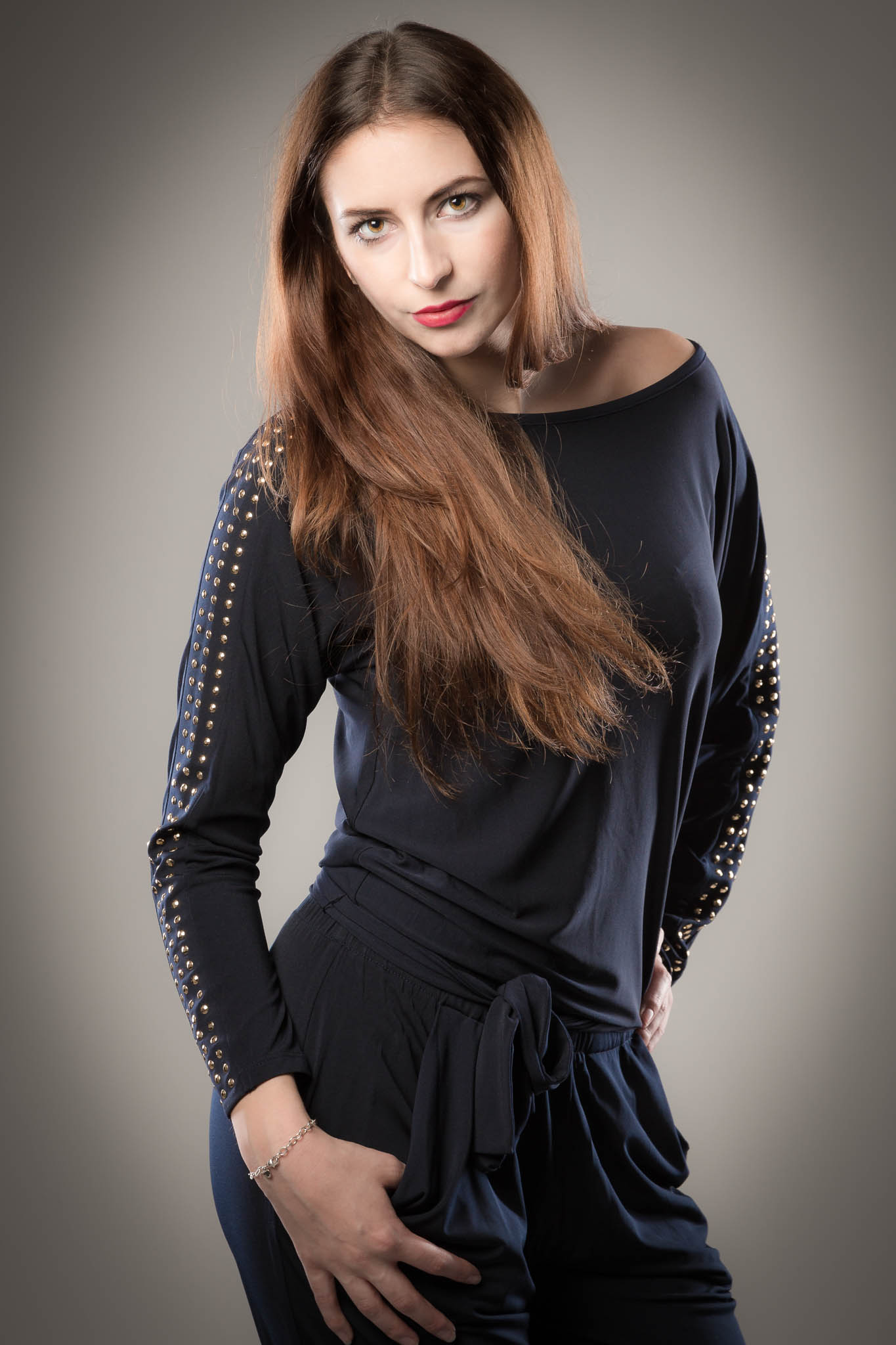 Woman in a stylish black outfit with gold studded sleeves, posing confidently against a gray background.