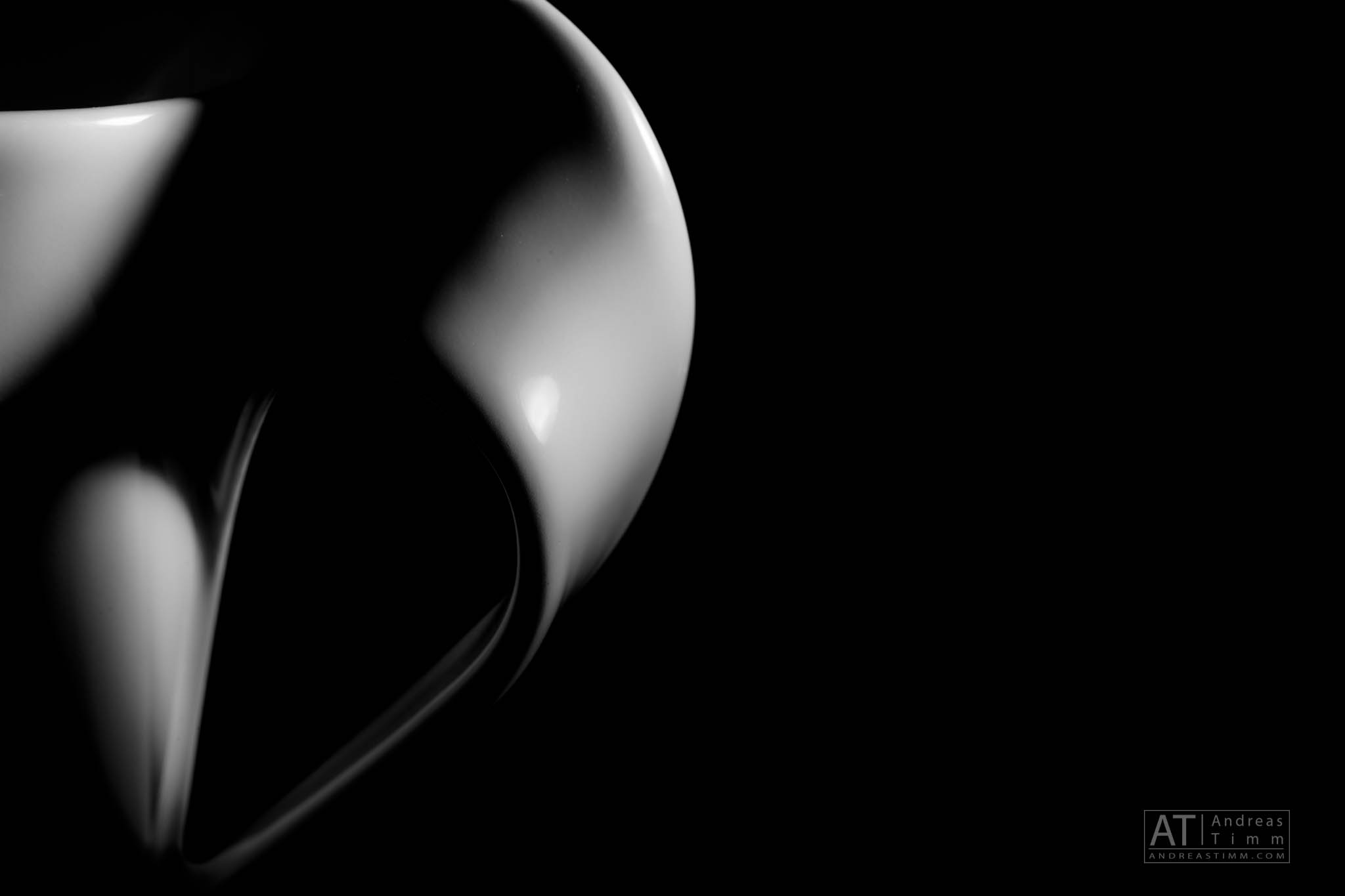 Abstract black and white photo of a curved, smooth object on a dark background, emphasizing light and shadow contrast.