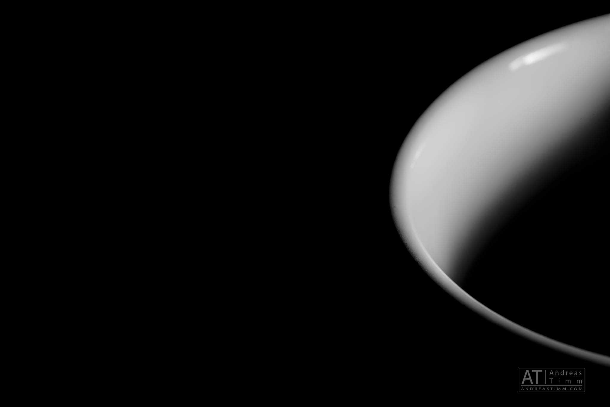Close-up of a white ceramic cup's curved edge against a black background, showcasing minimalistic contrast and sleek design.