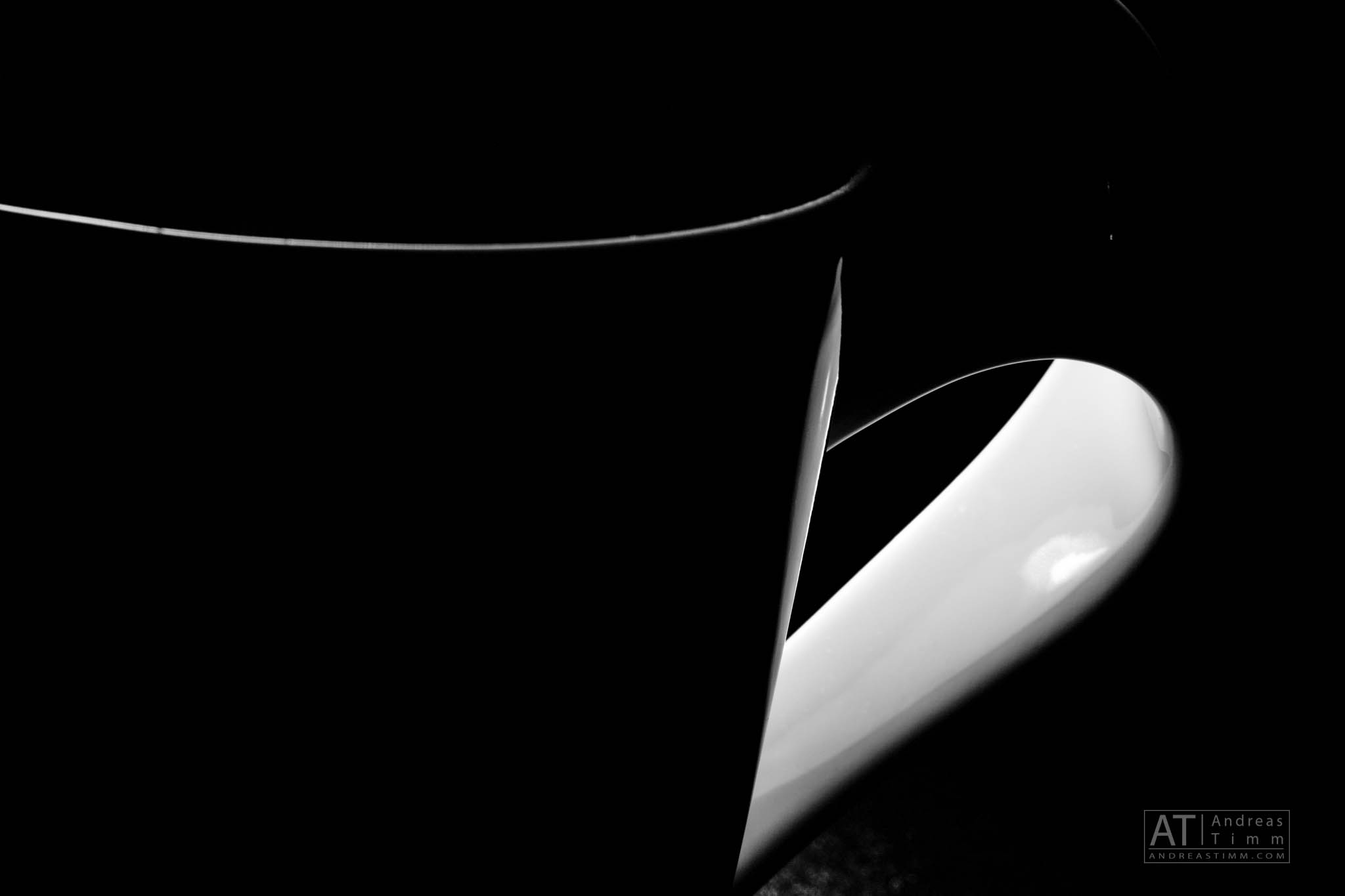 Close-up of a black and white coffee mug handle in dramatic lighting, highlighting sleek curves and contrast.