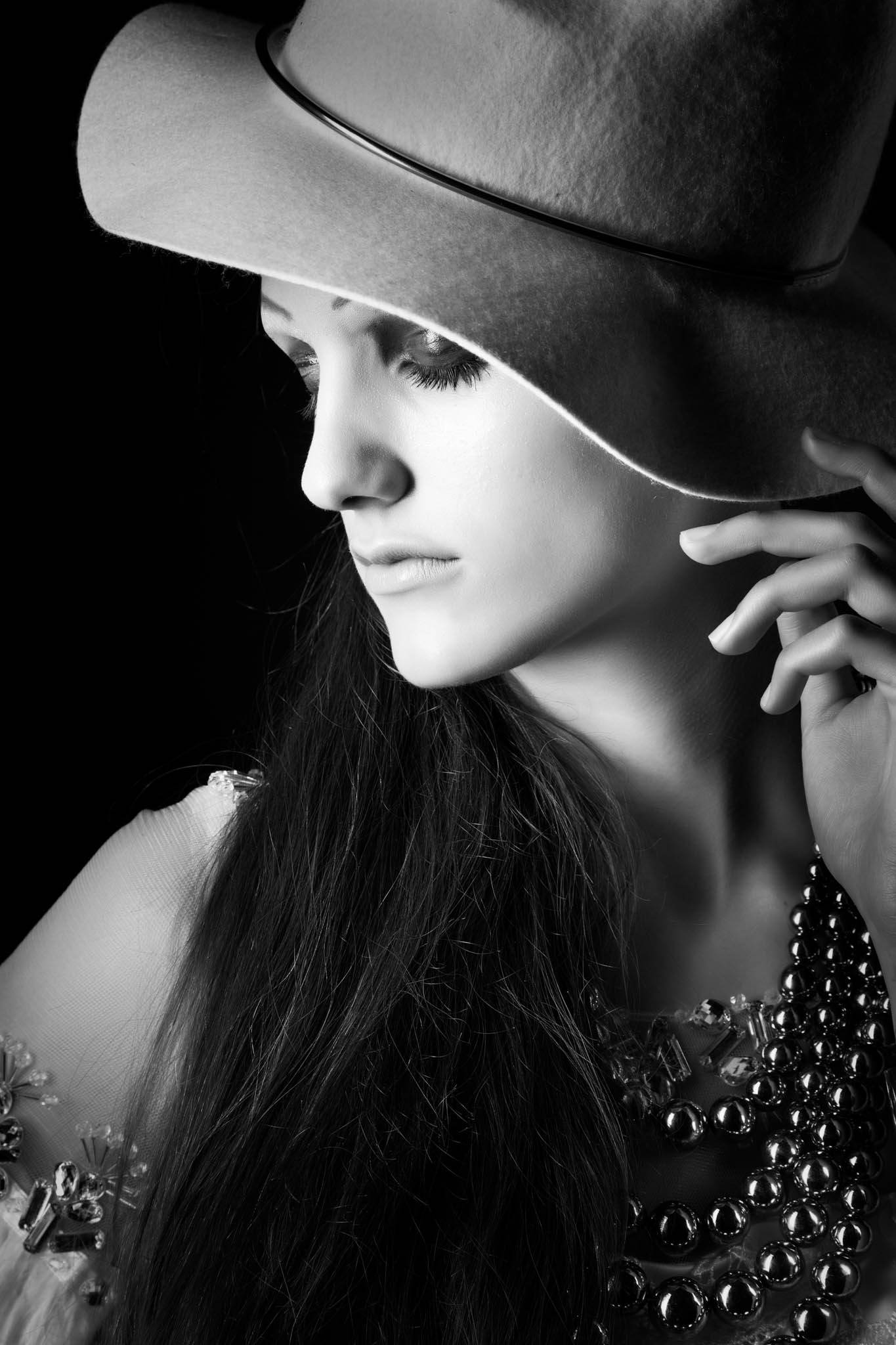Black and white portrait of a woman in a wide-brimmed hat, wearing a statement necklace.