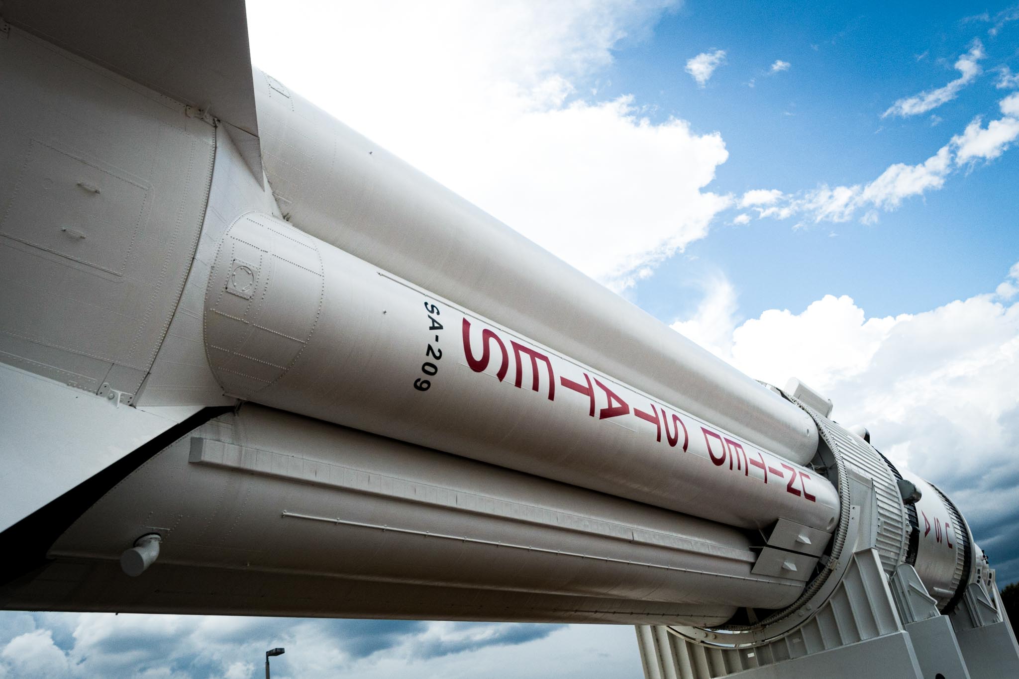 Close-up of a large white rocket with text, standing against a partly cloudy blue sky.