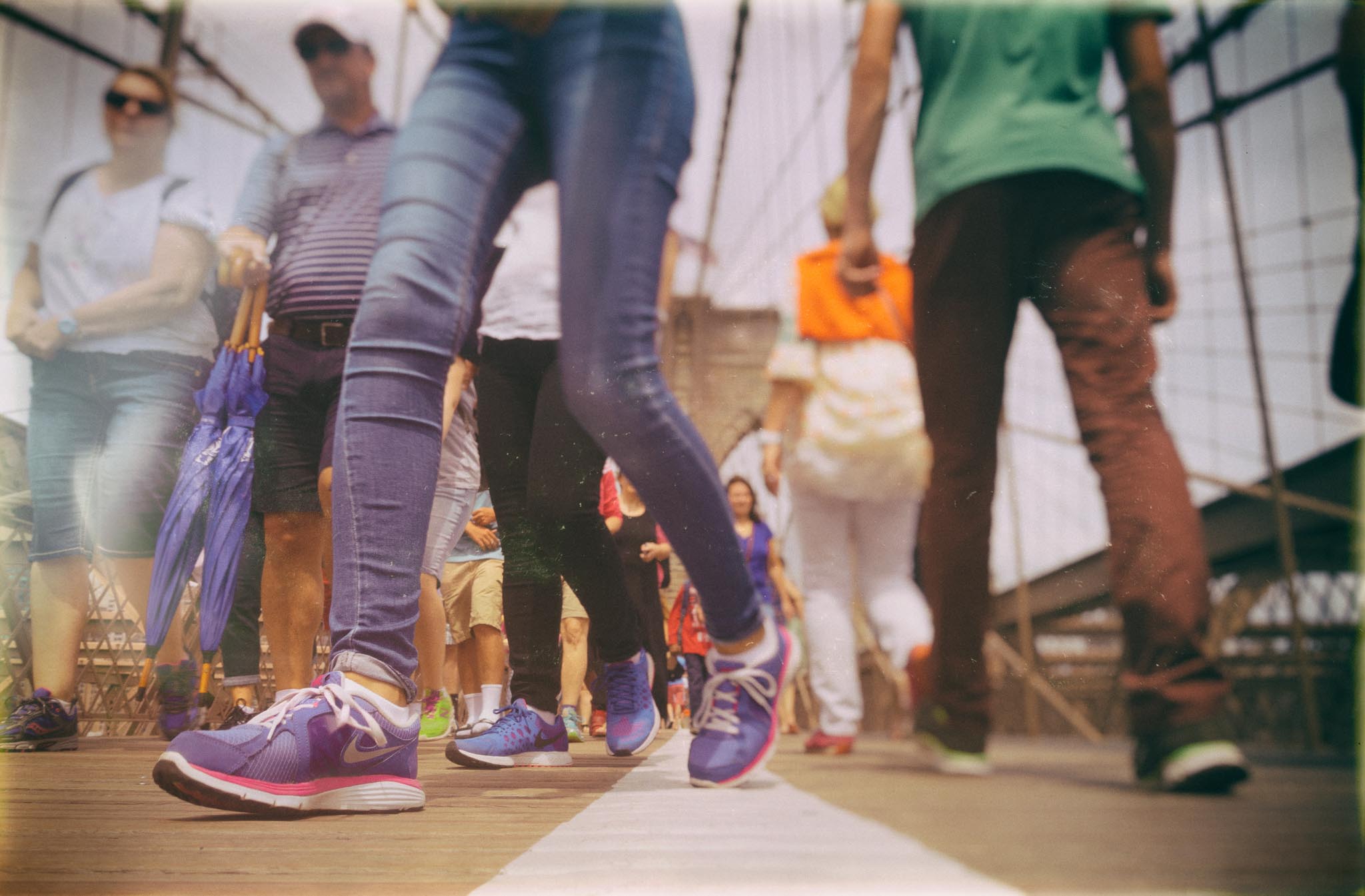 People walking on a busy bridge wearing colorful sneakers and casual clothing, viewed from a low-angle perspective.