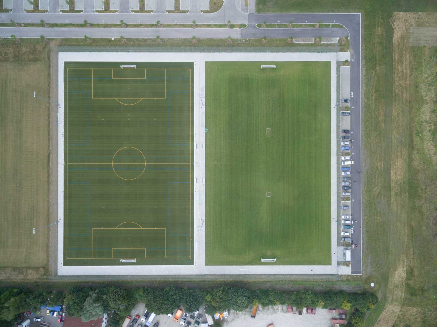 Aerial view of two adjacent football fields with marked lines and nearby parked cars.