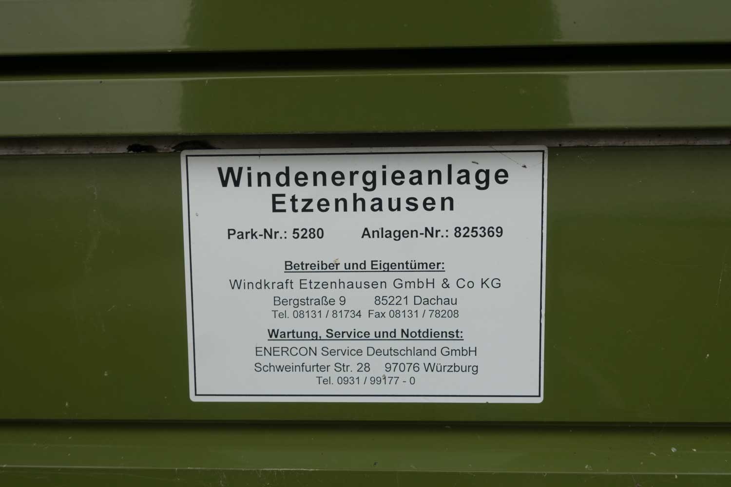 Sign with details for Windenergieanlage Etzenhausen on a green surface, showing contact info and service details.