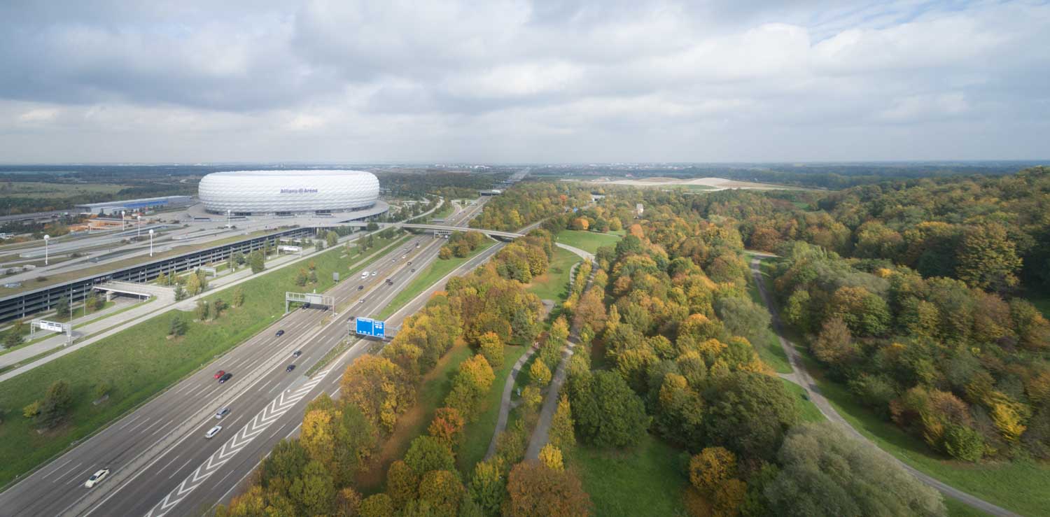 Aerial view of Allianz Arena with surrounding highways and autumnal forest landscape in Munich, Germany.