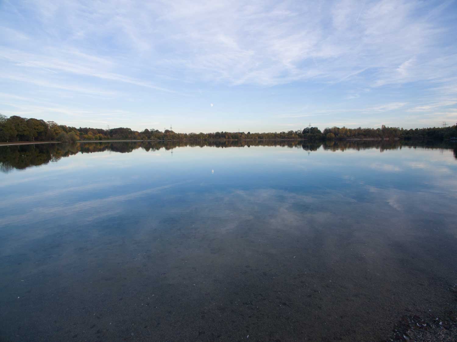Calm lake reflecting blue sky and distant trees on a clear day.