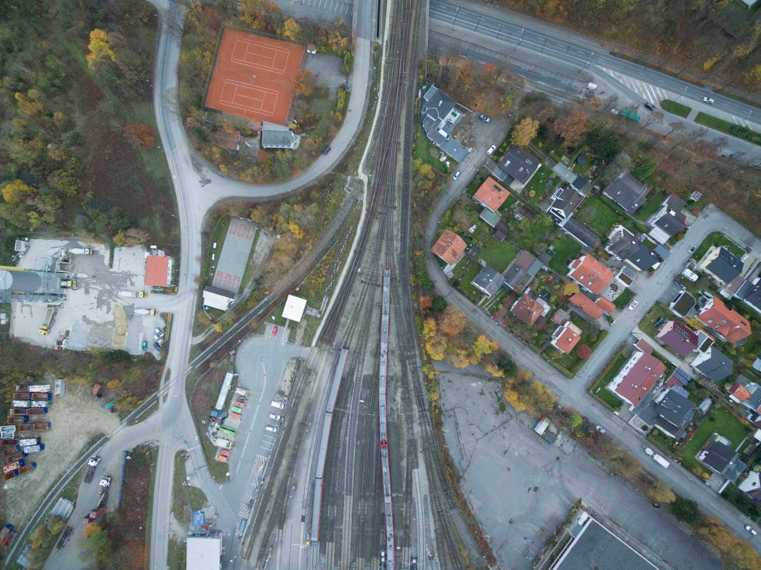 Aerial view of a railway intersection with nearby residential houses and orange tennis court surrounded by trees.