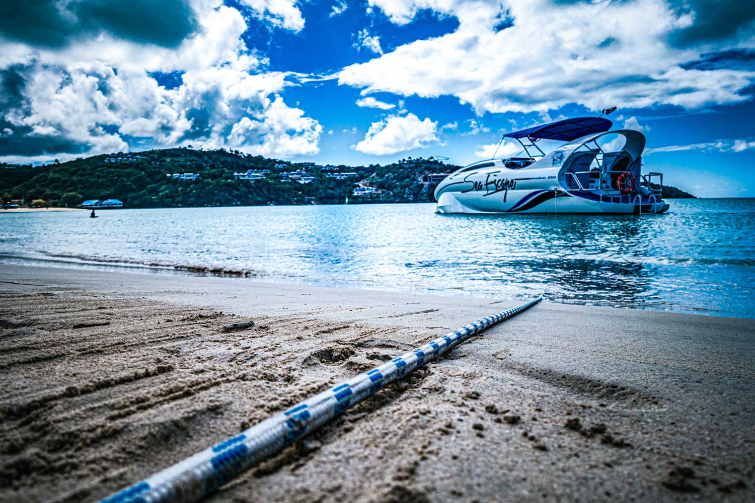 Speedboat anchored on a sandy beach with scenic hilly coastline in the background under a partly cloudy sky.