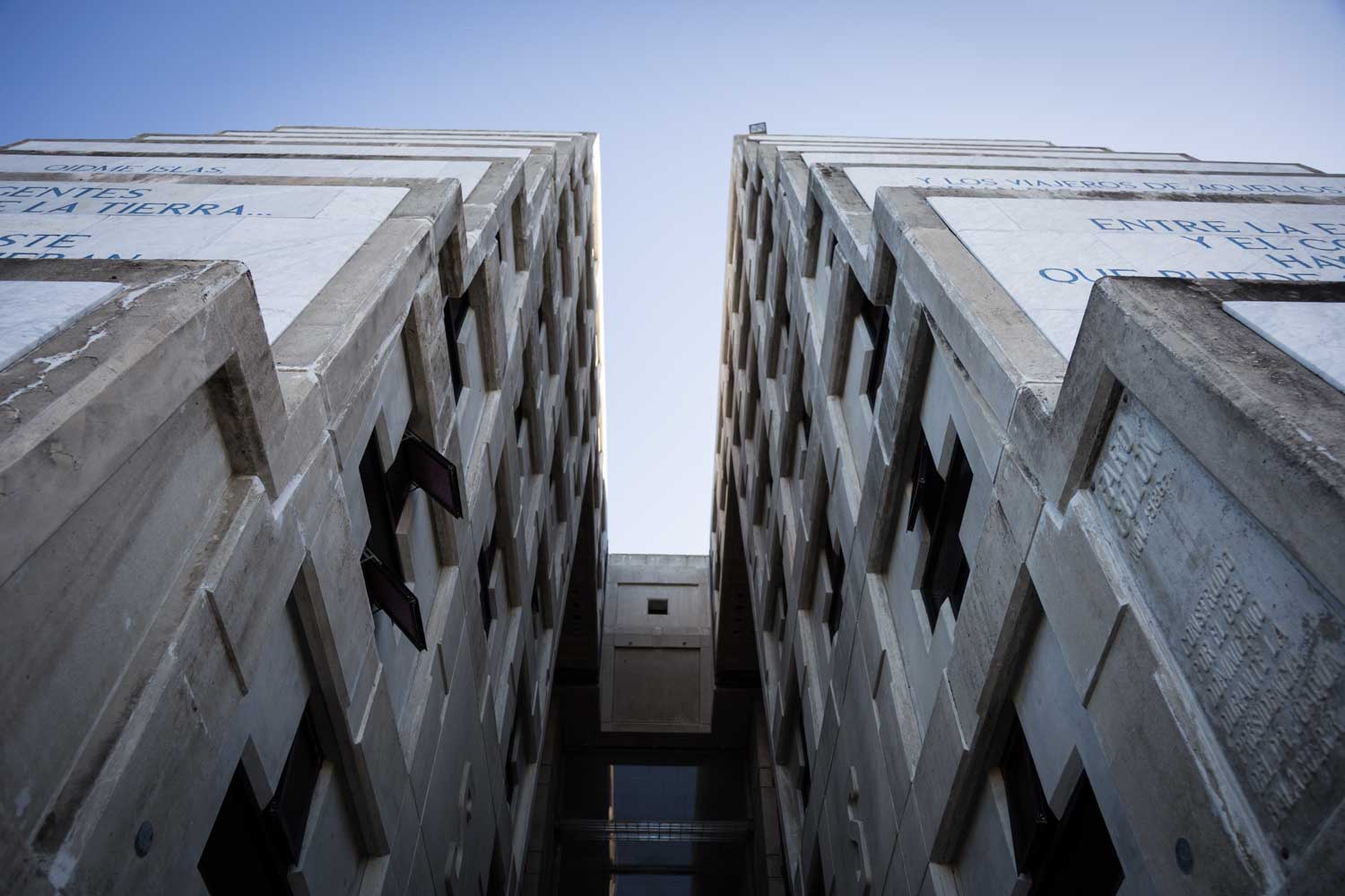 Symmetrical view between two tall, concrete buildings under a clear blue sky, with visible text and geometric details.