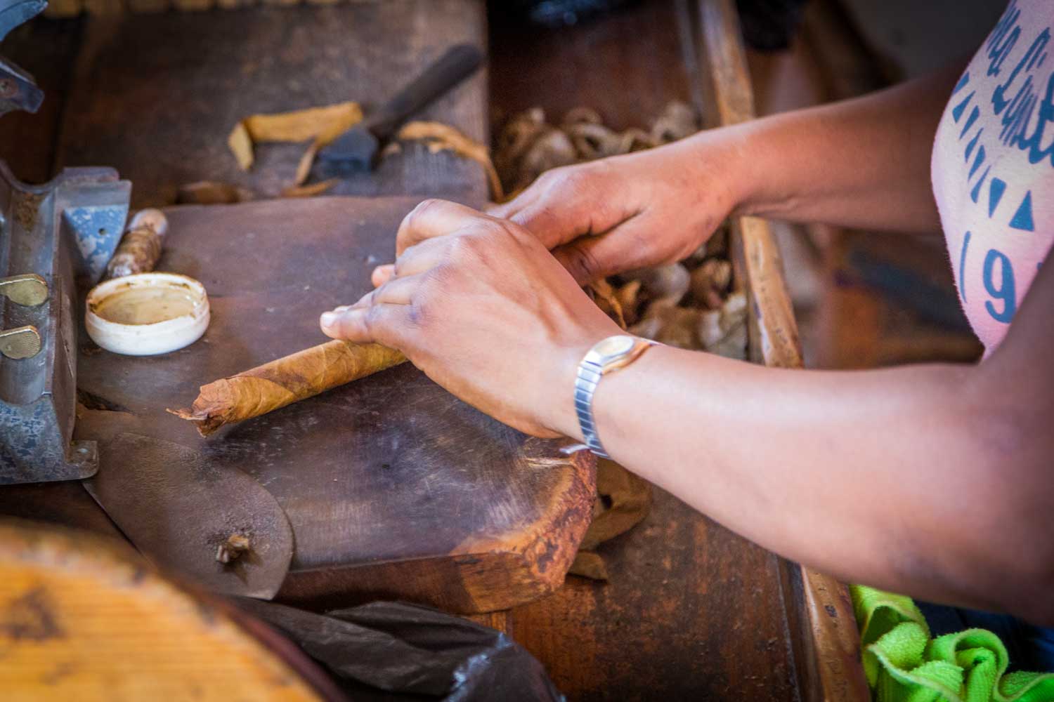 Person hand-rolling a cigar on a wooden table with tobacco leaves nearby.