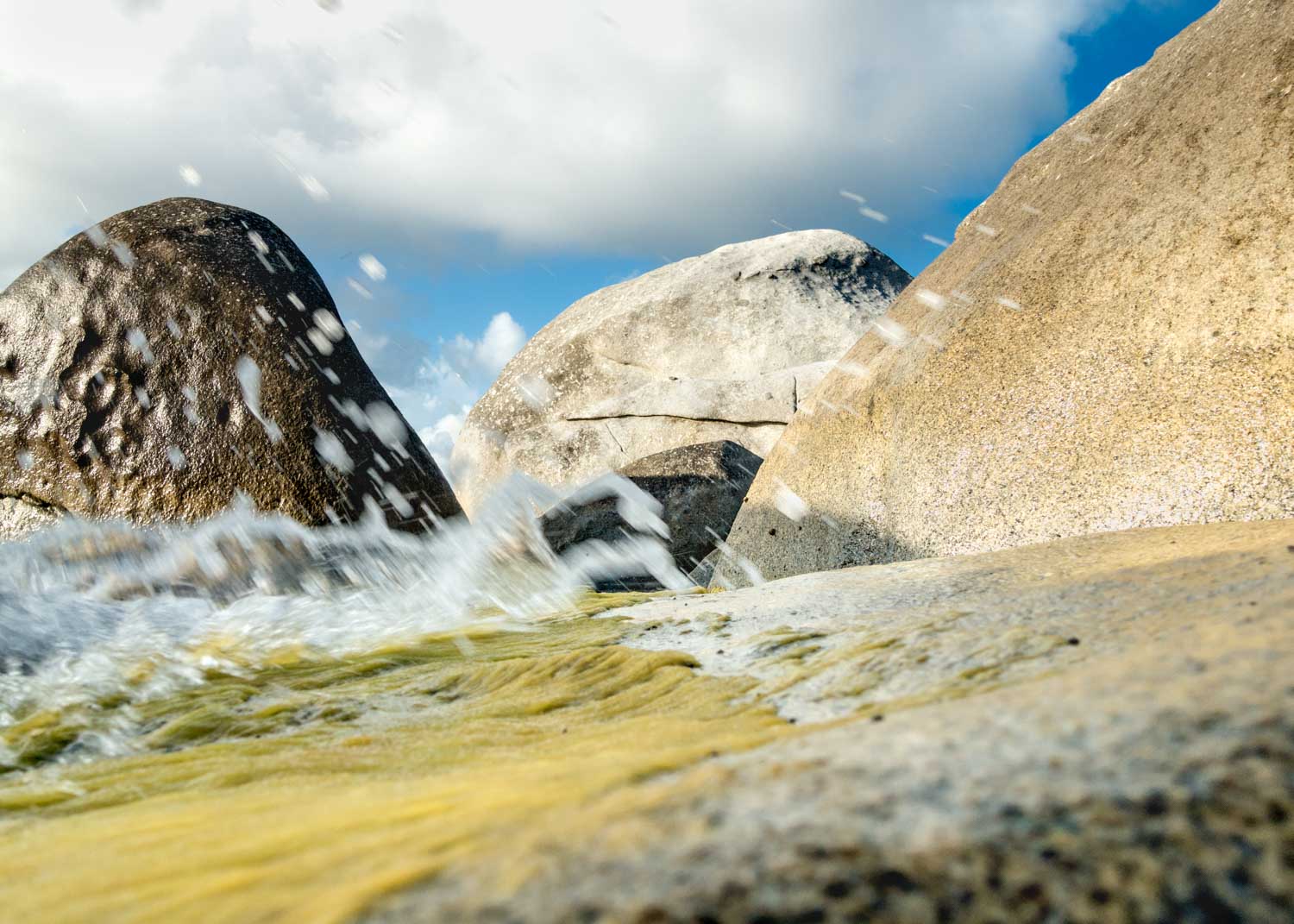 Waves splashing against large rocks under a partly cloudy sky, capturing coastal scenery and natural rock formations.