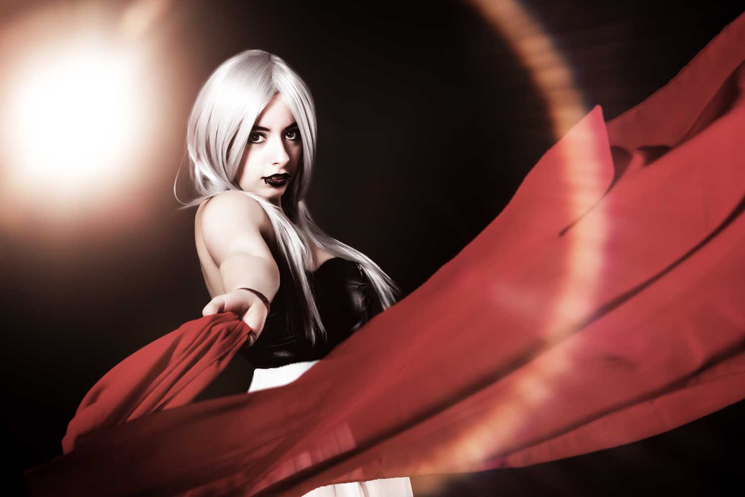Woman with long white hair and black lipstick holding a red scarf with dramatic lighting.