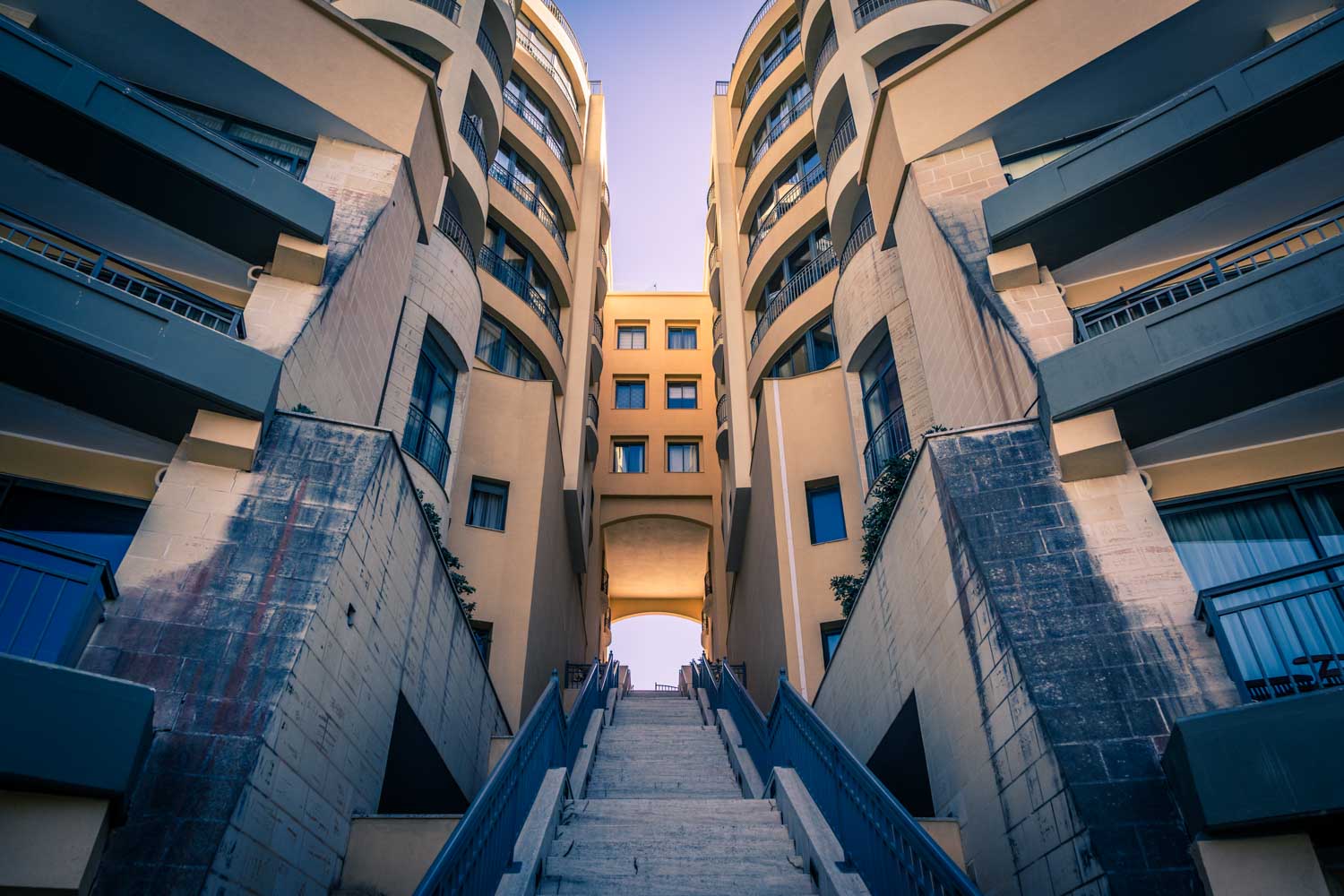 Wide staircase leading to modern beige buildings with balconies against a clear blue sky.