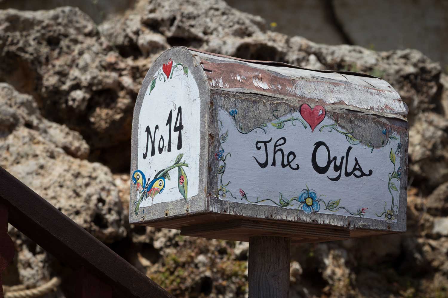 Decorated rustic mailbox with No. 14 and The Oyls, featuring floral and heart designs, against a rocky background.