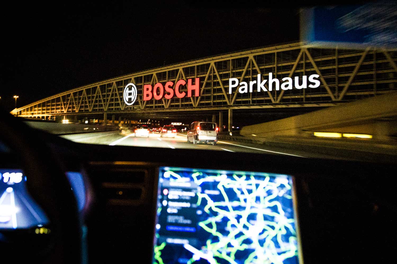 View from car at night showing Bosch Parkhaus sign over highway with illuminated GPS display in foreground.