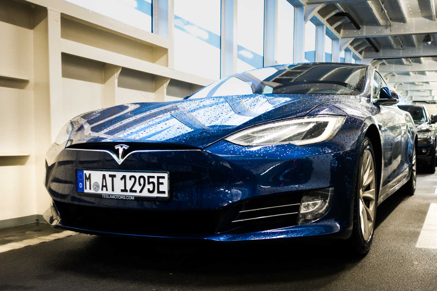 Blue Tesla Model S parked indoors with raindrops on hood, showcasing sleek design and modern headlight features.