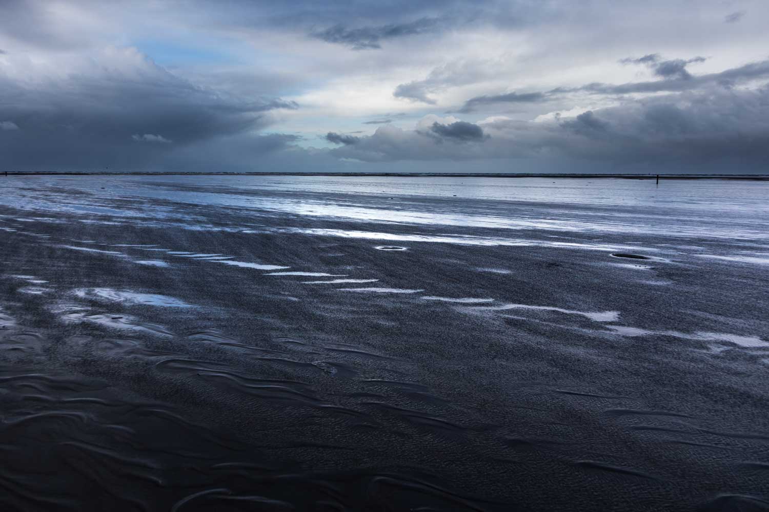 Stormy gray sky over a reflective, wet sandy beach. Moody seascape with dark clouds in the distance.