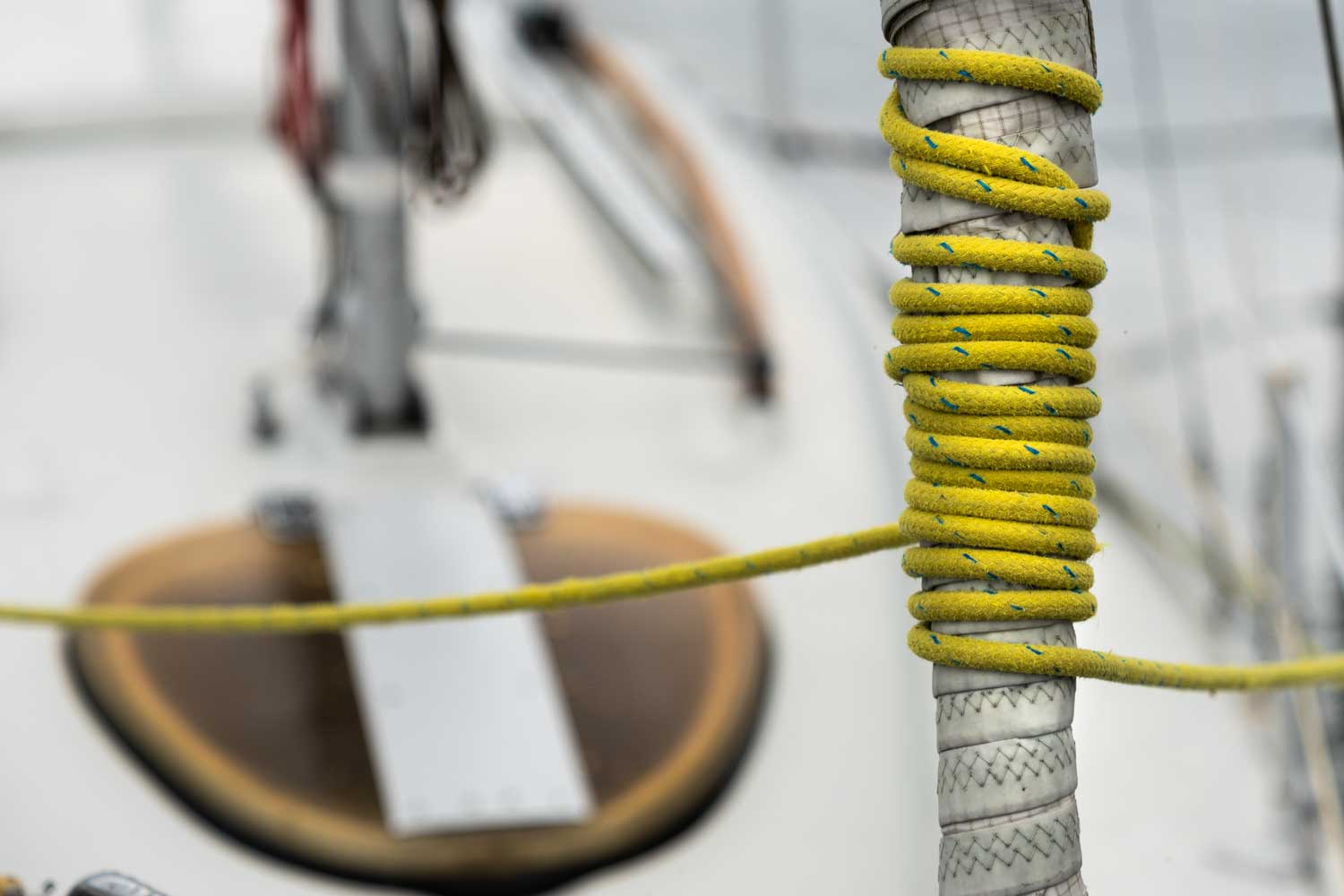 Yellow rope coiled around yacht post with blurred deck background, capturing nautical details on a boat.
