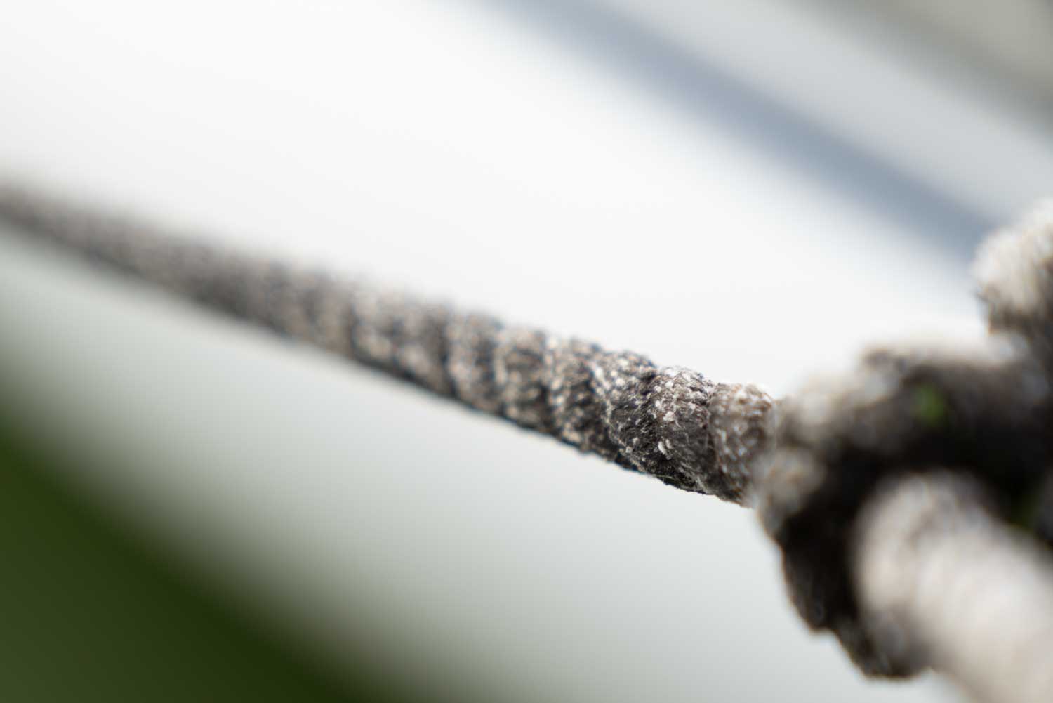 Close-up of a textured brown rope in focus, stretching diagonally against a blurred white and green background.
