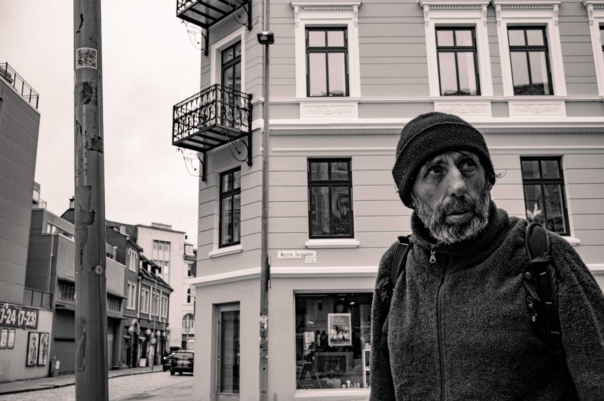 Man in winter clothing on urban street corner with historic building, black and white photography.