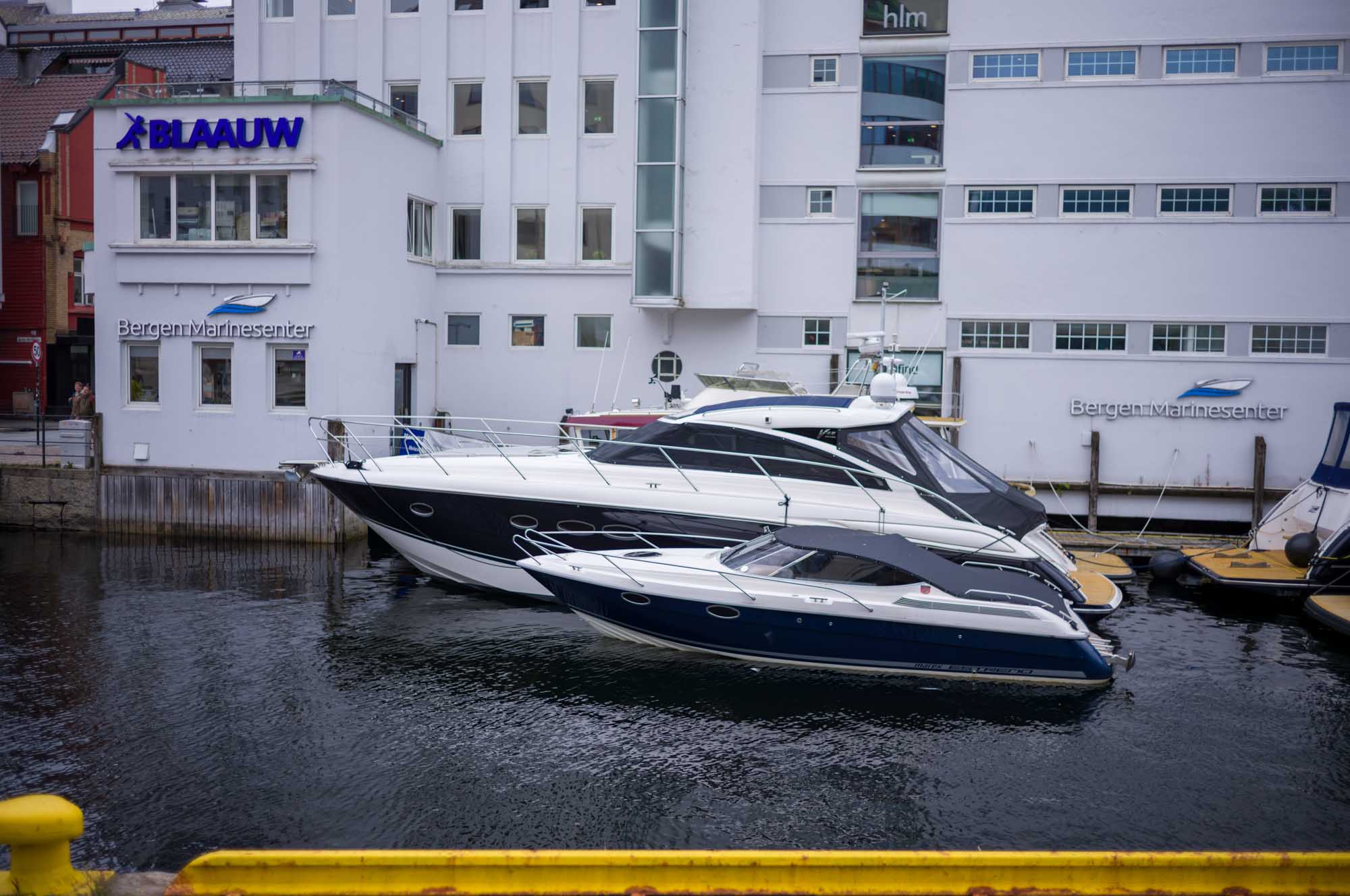 Two sleek yachts docked by a building labeled Bergen Marinesenter on a waterfront.