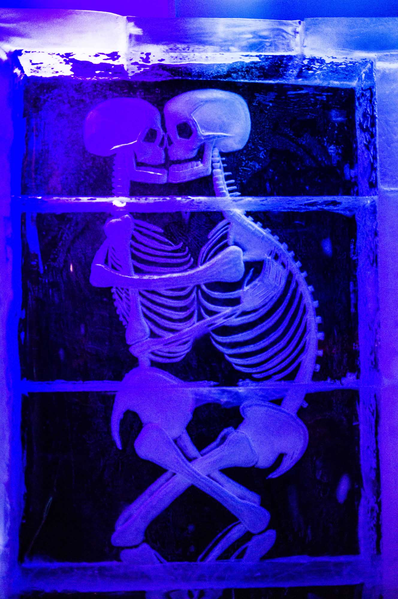 Two skeletons carved in ice embrace under blue light, creating a unique artistic scene.
