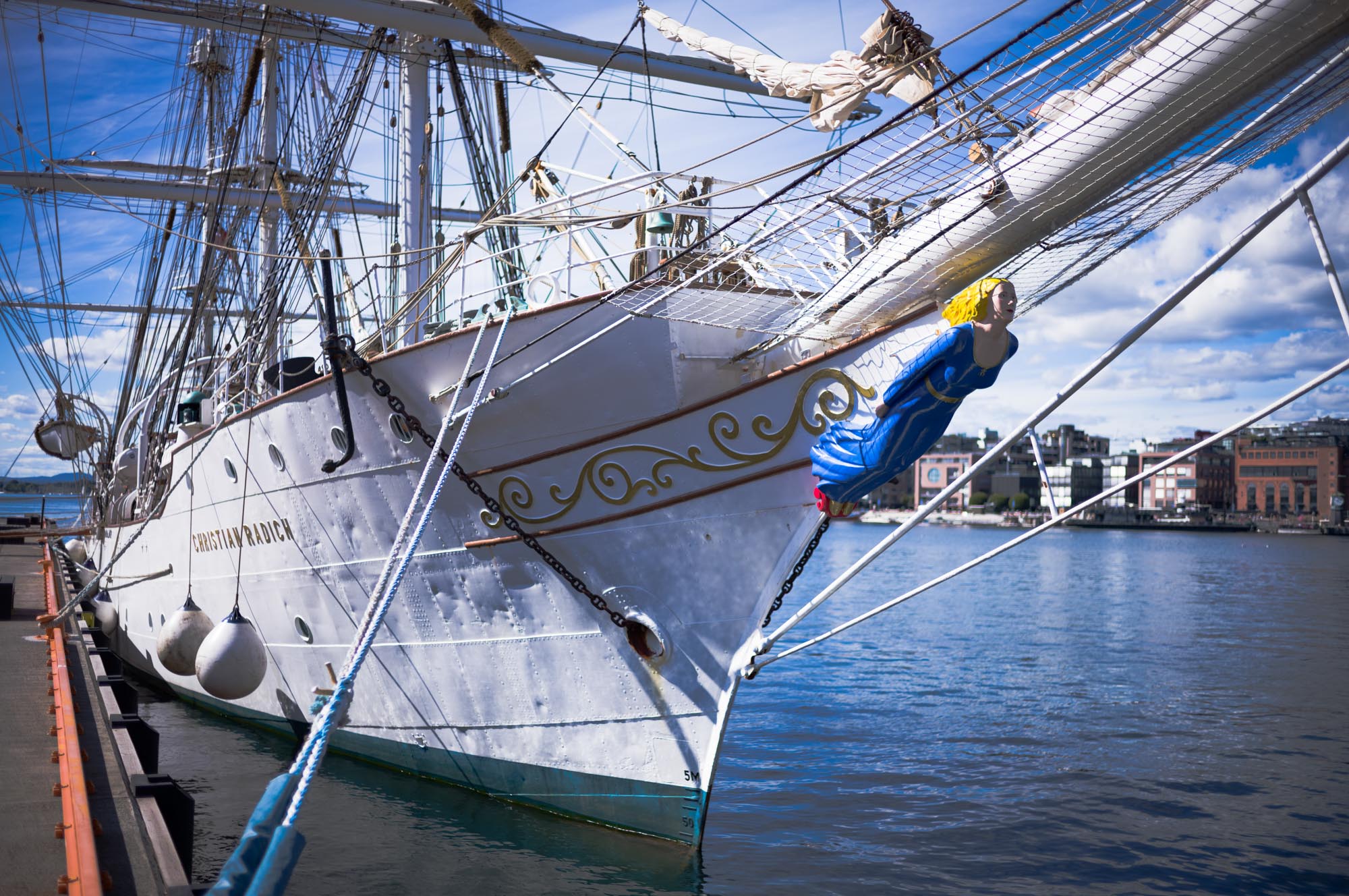 White sailing ship docked with ornate figurehead under blue sky.