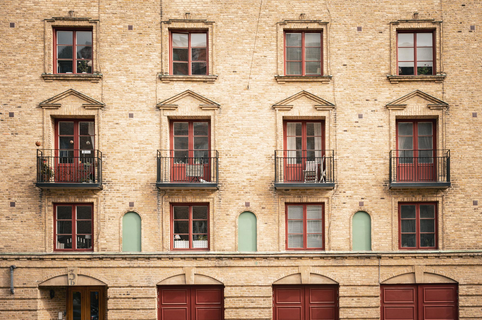 Brick building facade with red windows and doors, balconies, and decorative arches.