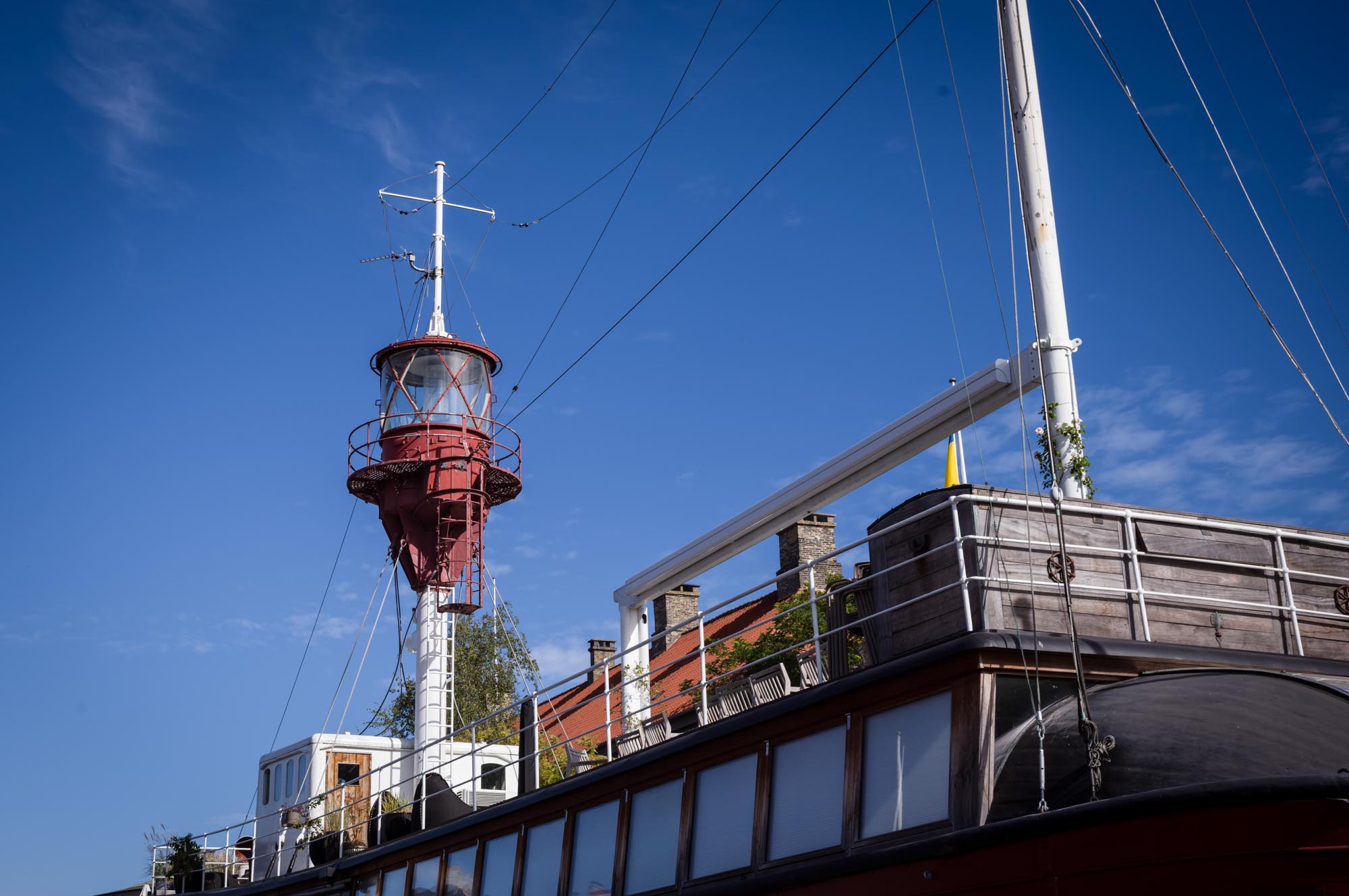 Vintage ship with red lighthouse structure against clear blue sky.