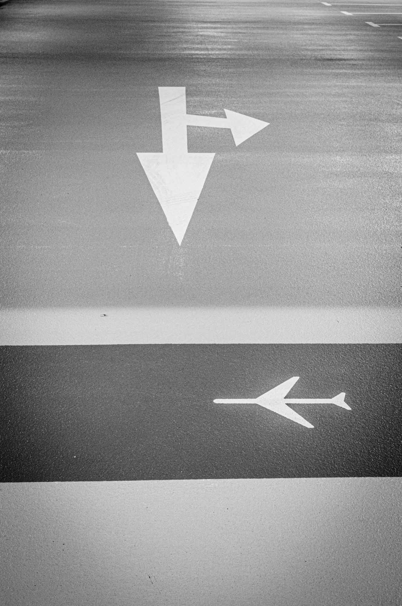 Black and white road markings with arrows pointing forward and left, and an airplane symbol for direction.