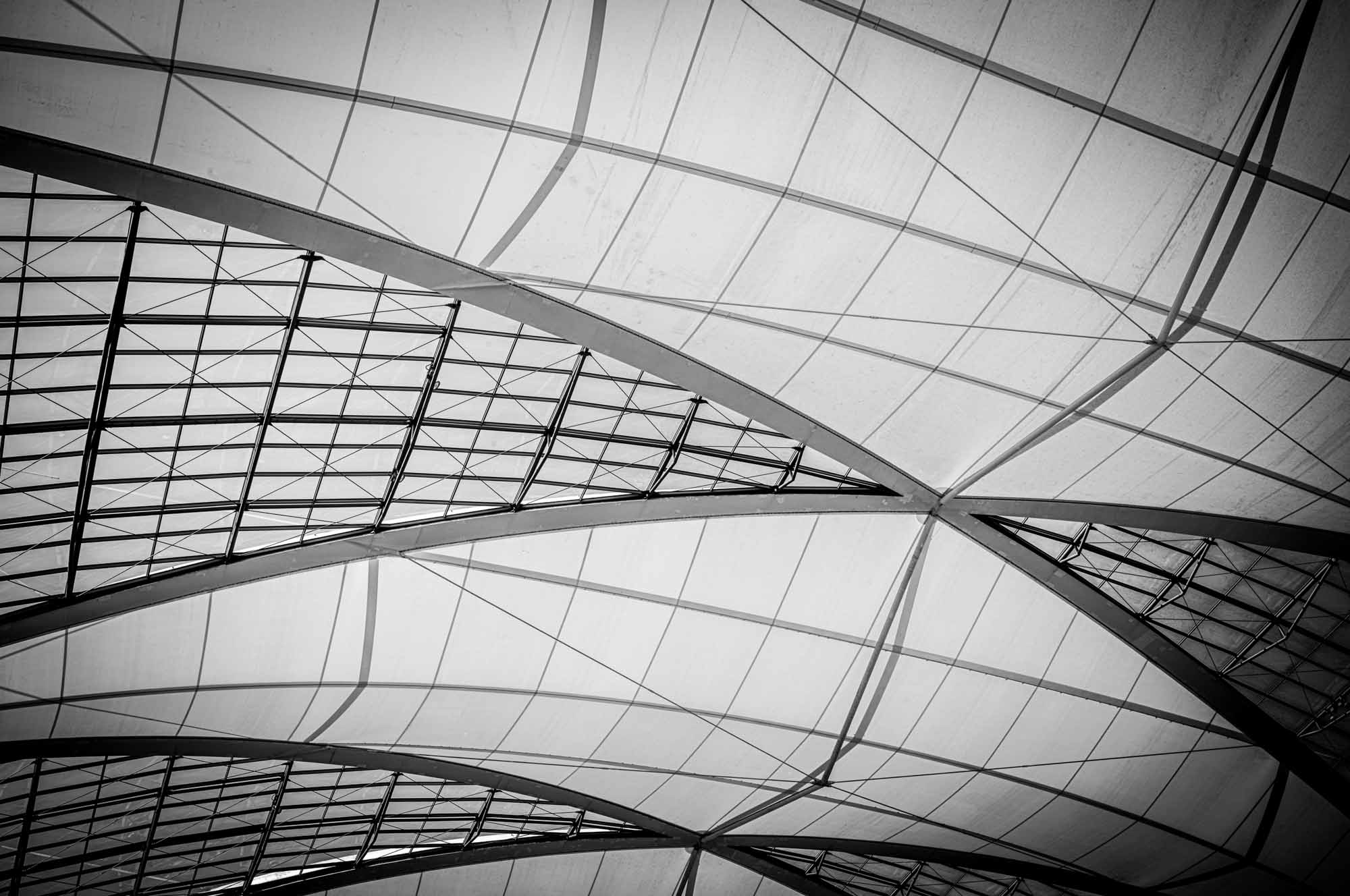 Geometric architectural ceiling with intersecting beams and grid pattern, creating modern, abstract lines in monochrome.