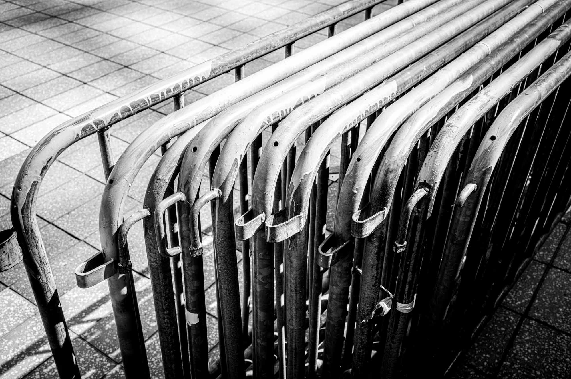 Row of metal barricades aligned on tiled ground, shown in black and white, creating a pattern of curves and lines.