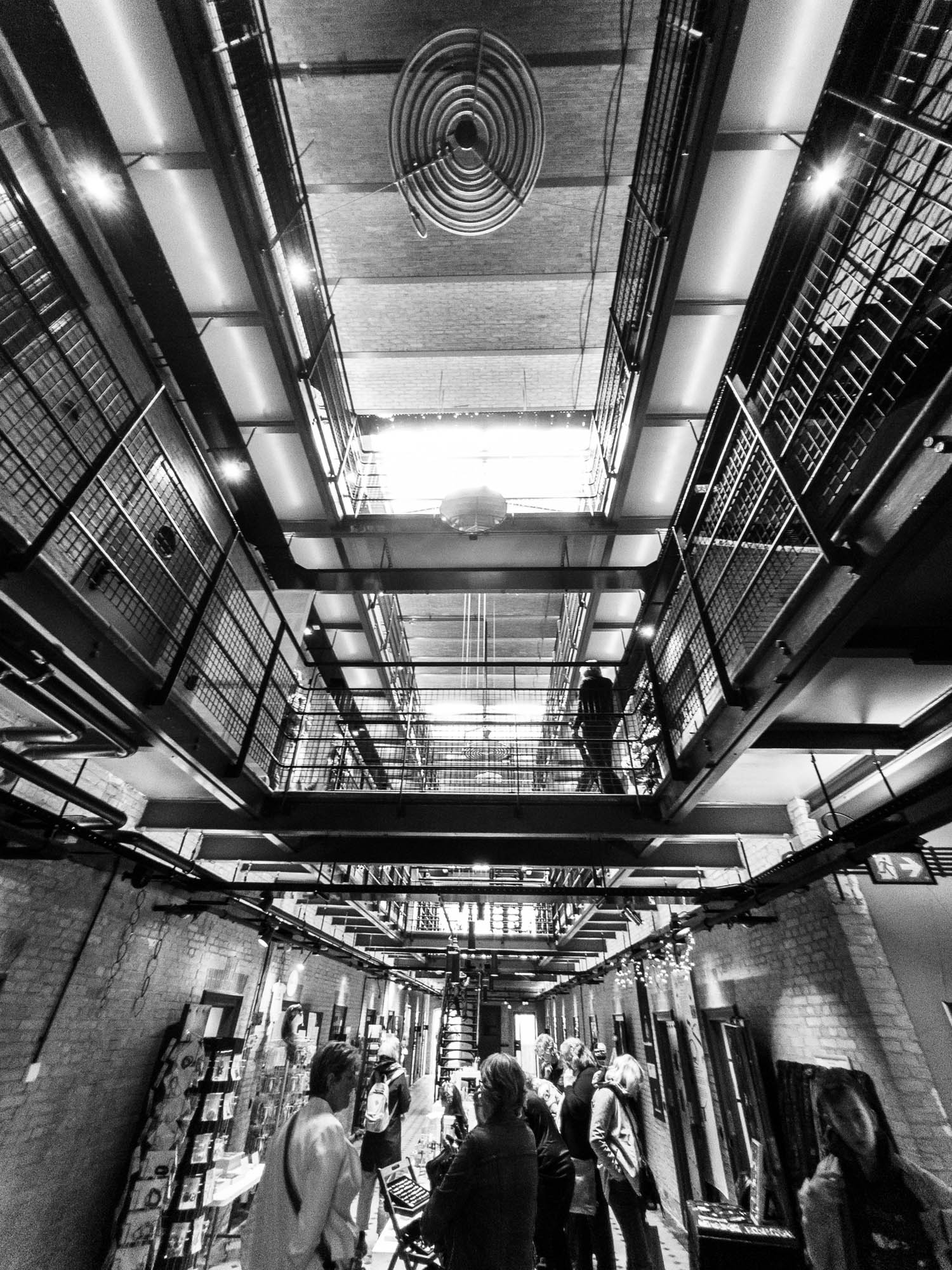 Black and white photo of people inside a modern, industrial-style building with high ceilings and metal walkways.