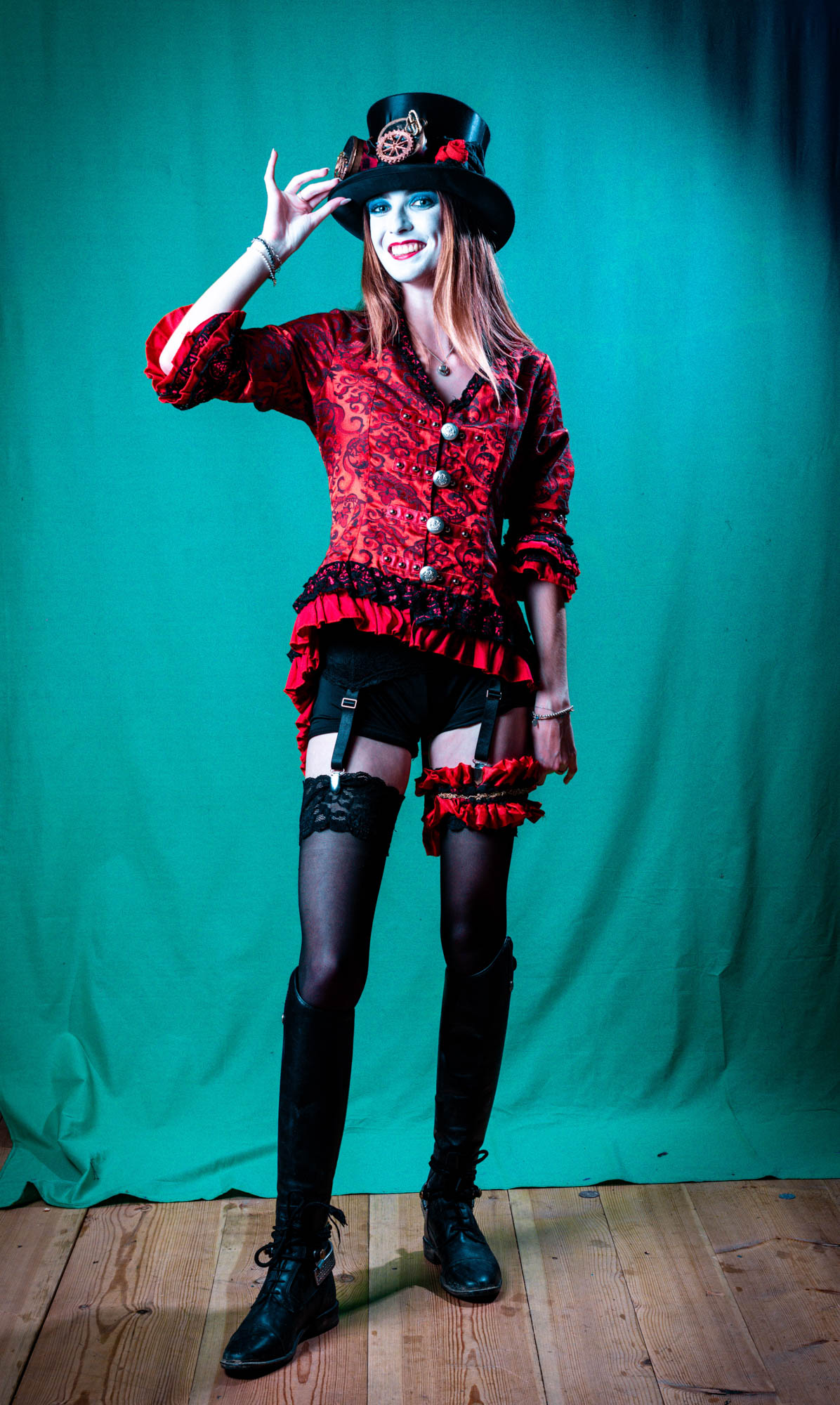 Woman in vibrant steampunk attire with top hat and corset poses against a green backdrop.
