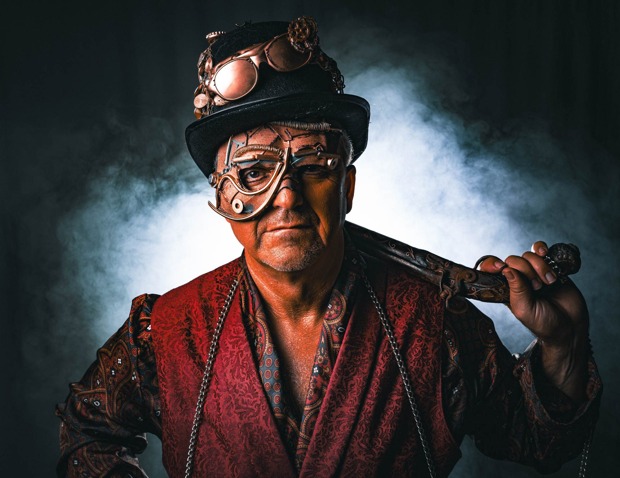 Steampunk man in detailed costume with top hat and mask, holding a cane against a smoky backdrop.