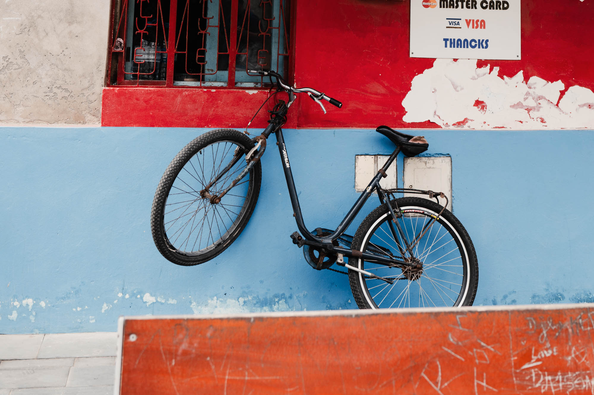 Black bicycle leaning against a colorful red and blue wall with a vintage vibe.