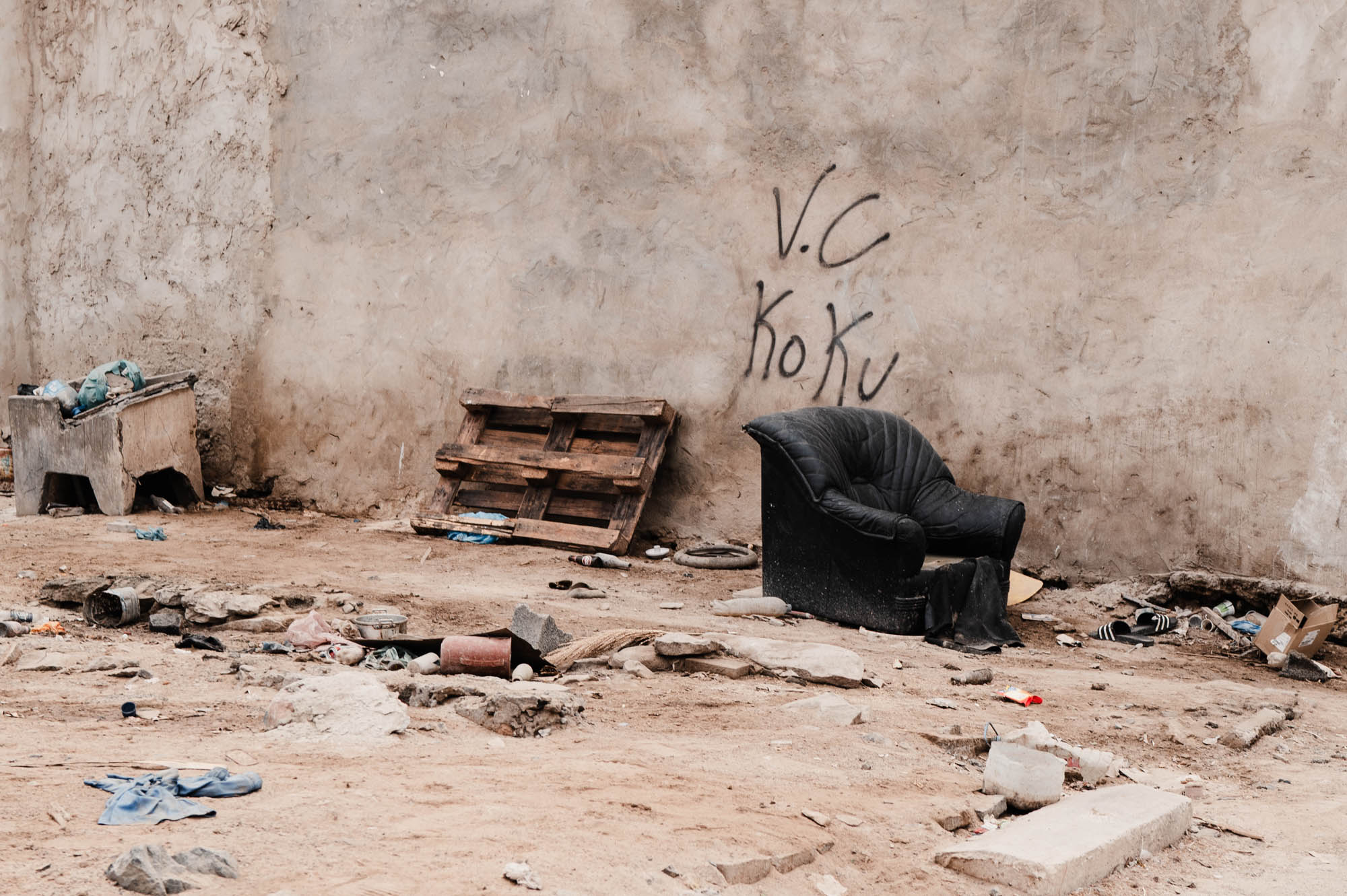 Abandoned area with discarded chair, graffiti, and debris against a concrete wall, symbolizing urban decay.