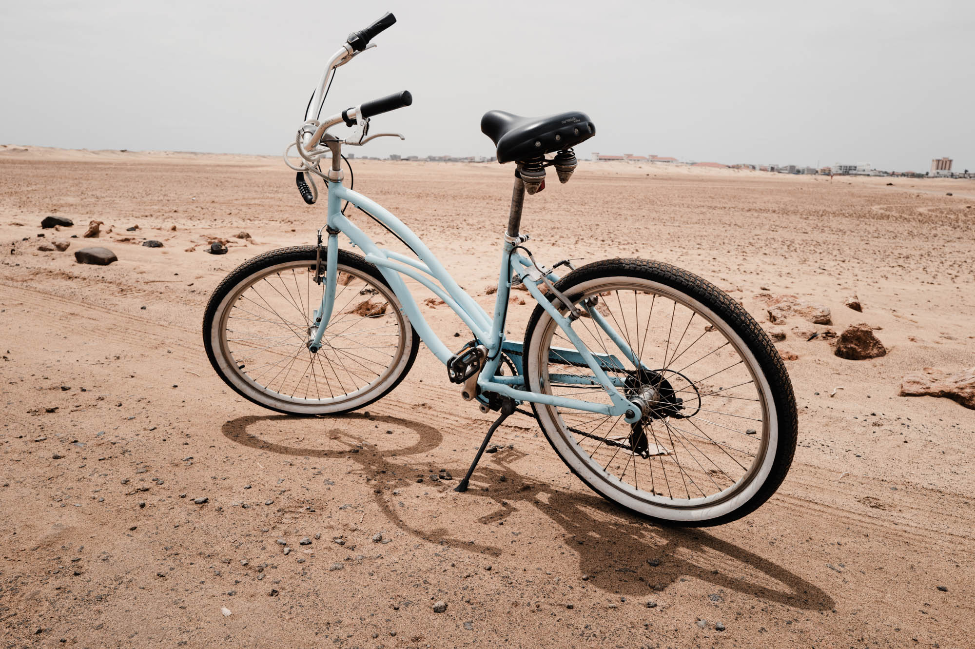 Blue vintage bicycle standing on sandy desert landscape under cloudy sky.